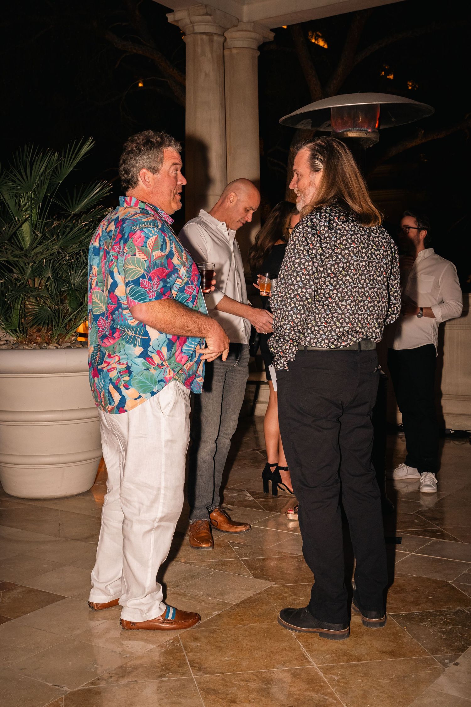 Person in colorful tropical shirt engaging in animated conversation at an elegant evening event.