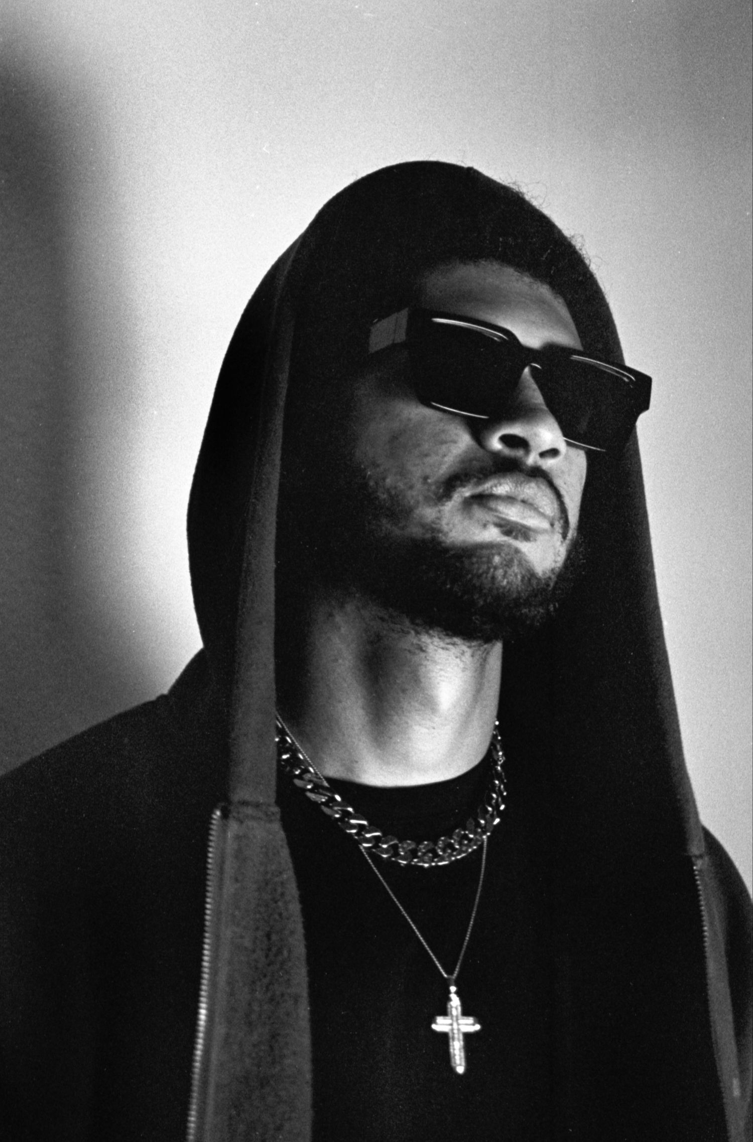 Dramatic black and white portrait of person in hooded garment wearing jewelry.