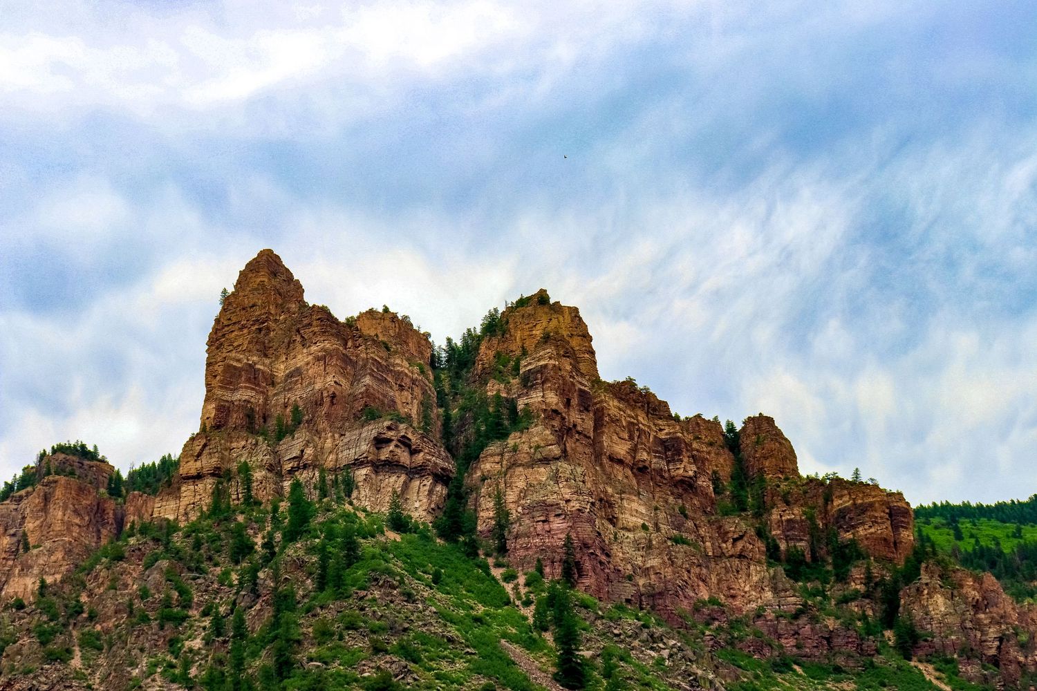 Rugged red rock formations rise against cloudy sky in mountainous landscape.