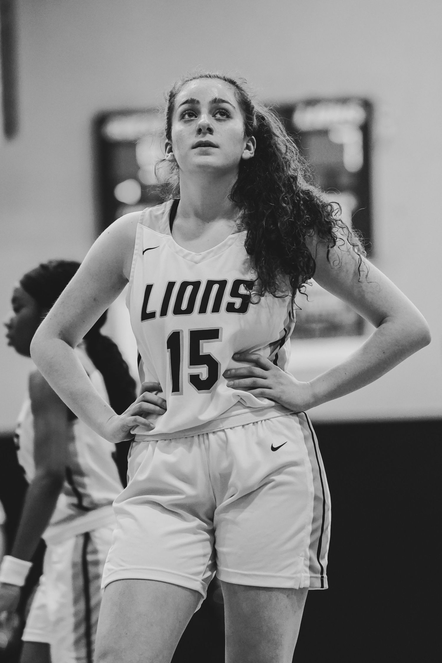 Basketball player in white Lions jersey number 15 standing on court in black and white photo.