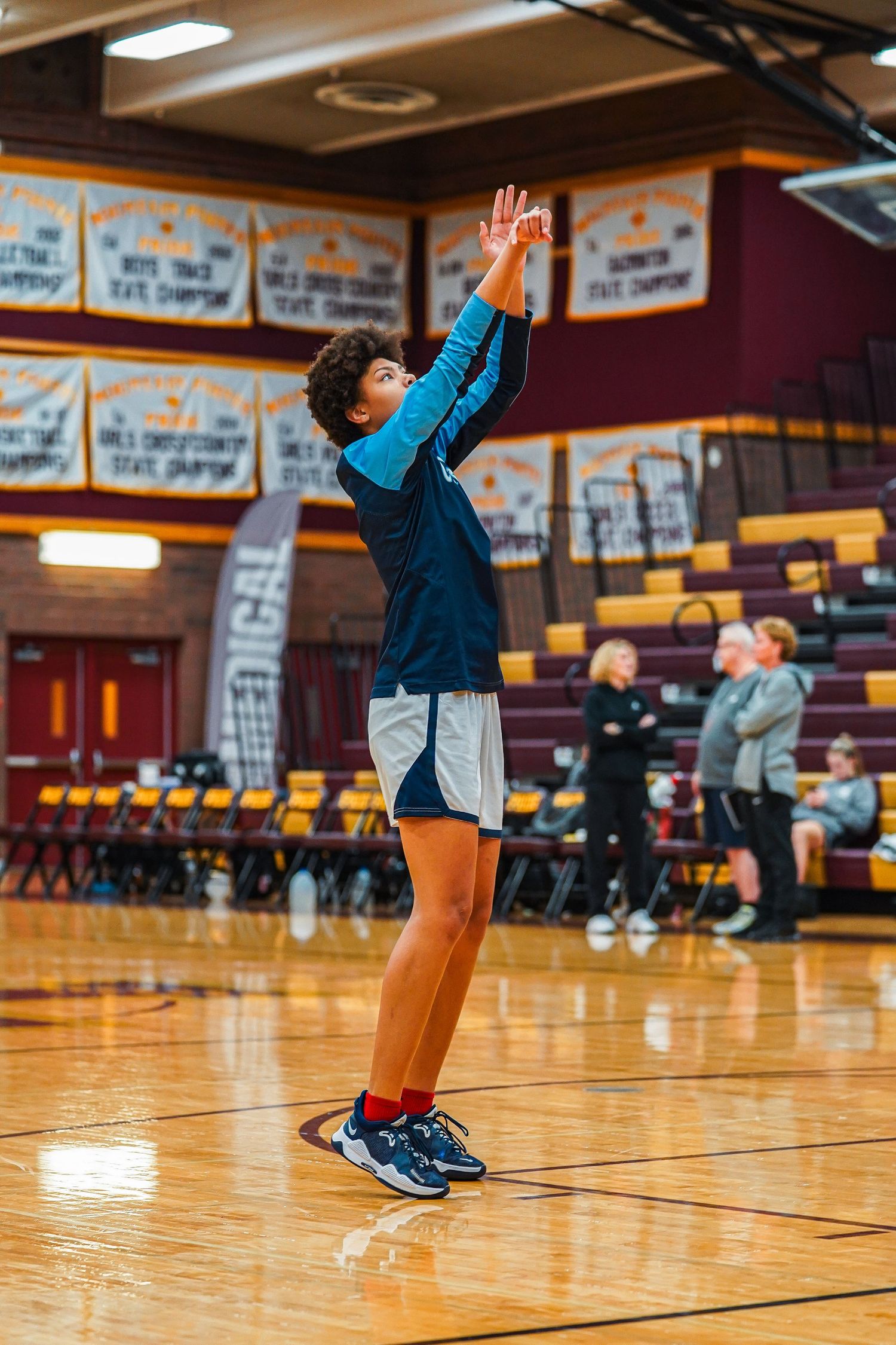 Young athletes perform jumping and stretching exercises in a basketball gymnasium.