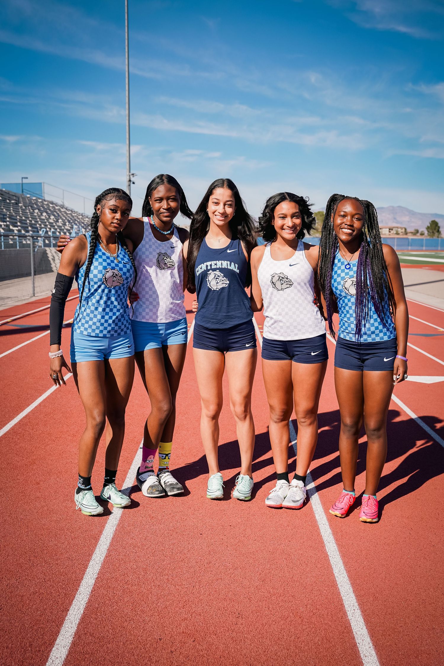 Track team poses together wearing blue and white uniforms on outdoor track.