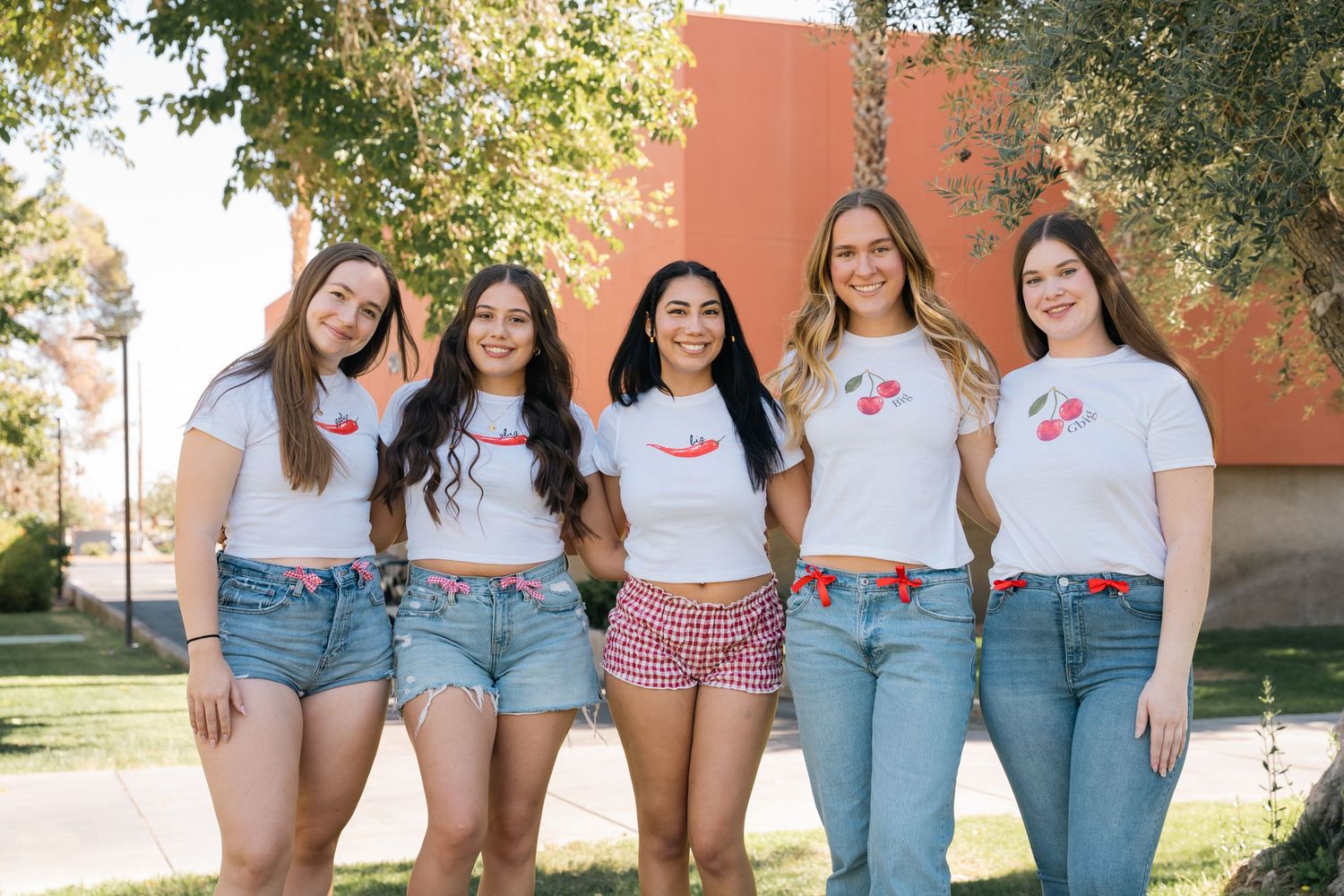 Five friends in coordinated white t-shirts and denim shorts pose against outdoor wall.