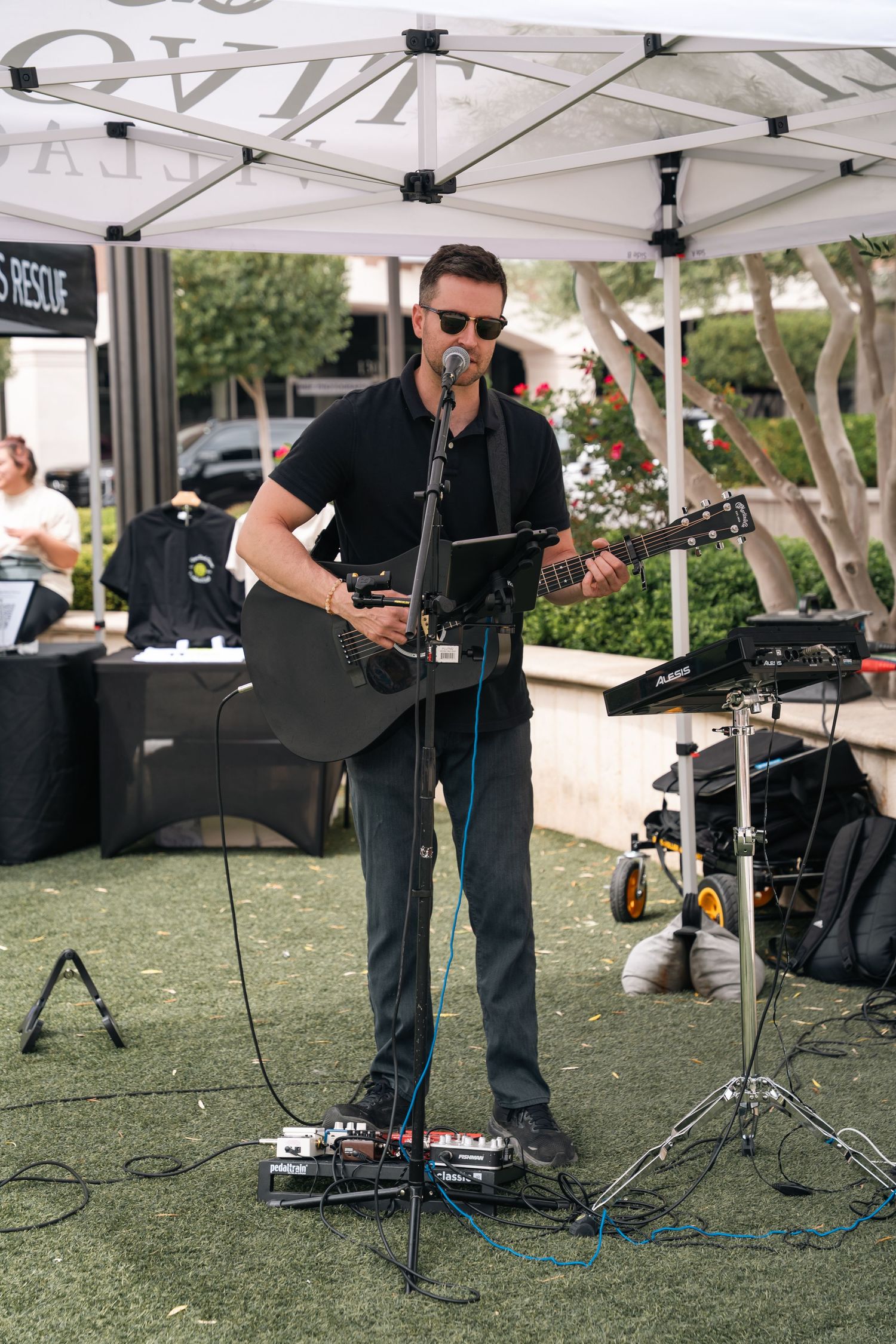 Musician performing with acoustic guitar under white canopy tent at outdoor event.