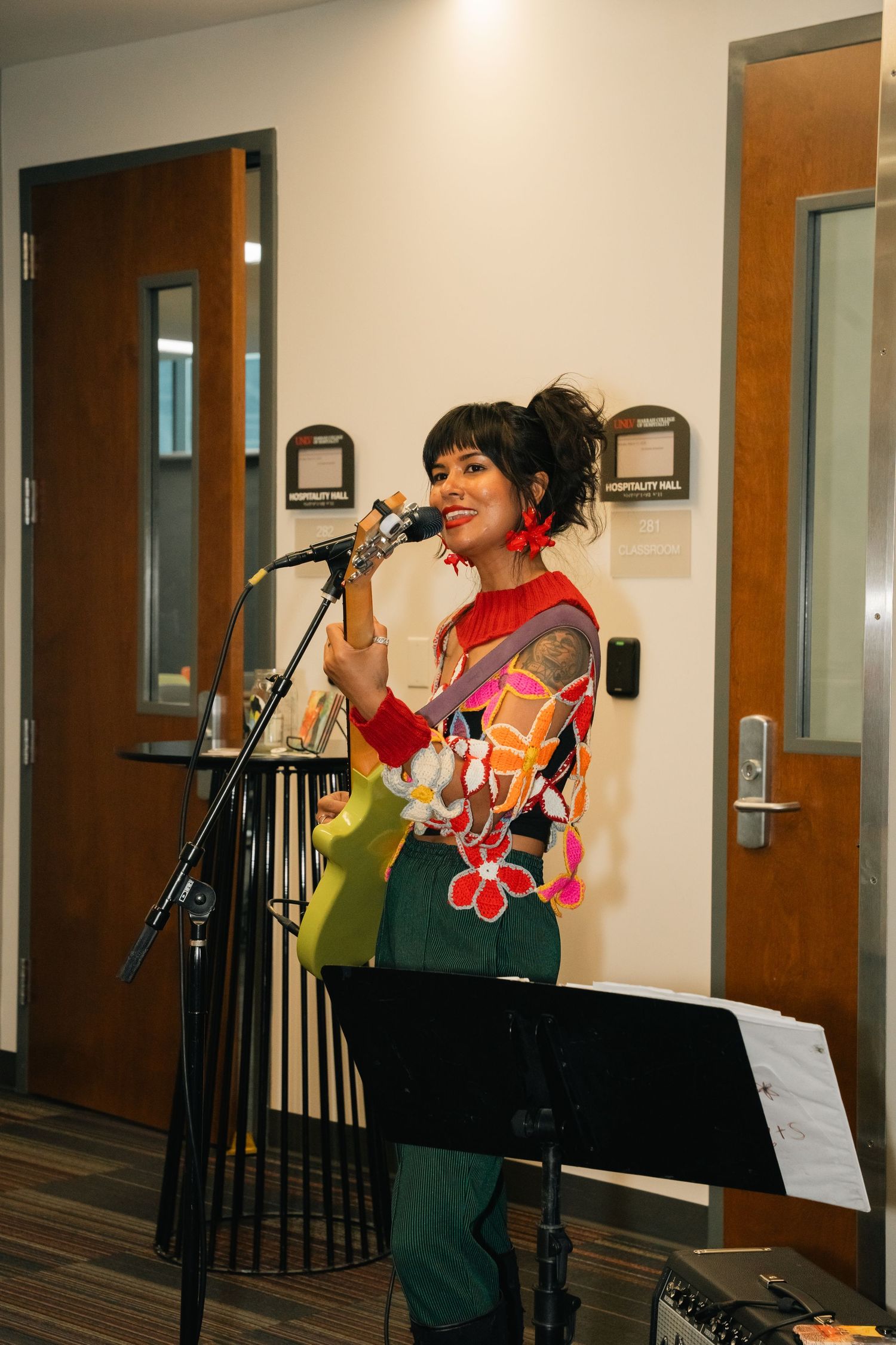 Performer in colorful outfit singing at microphone against neutral background.
