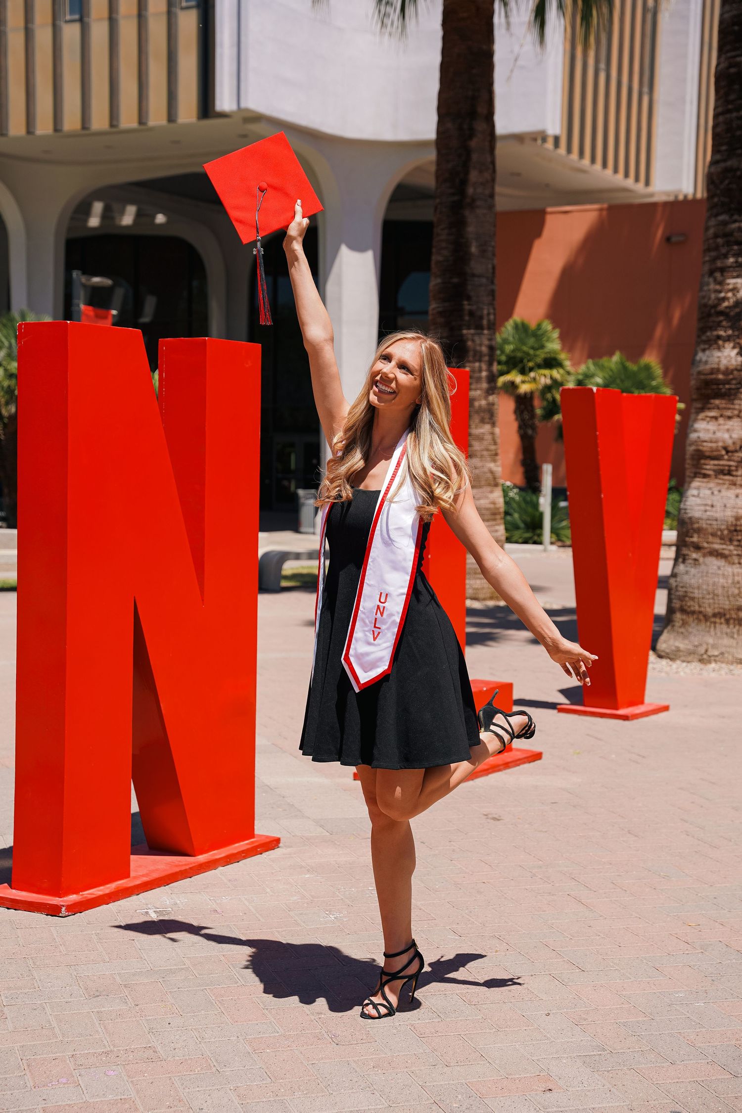 Graduate celebrates by large red letters holding cap during graduation photoshoot.