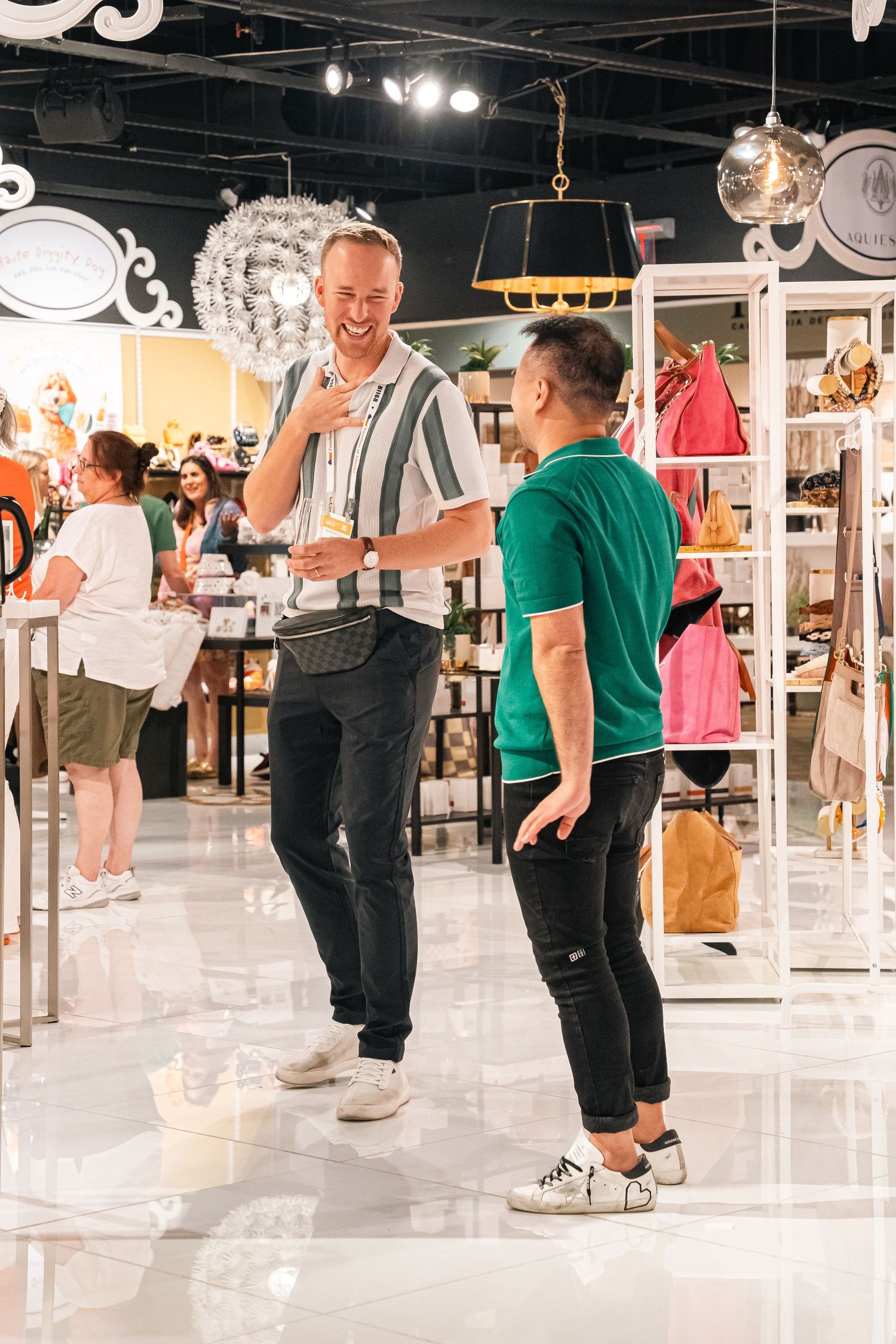 Two shoppers chat and browse merchandise in a retail store with lighting fixtures and clothing displays.