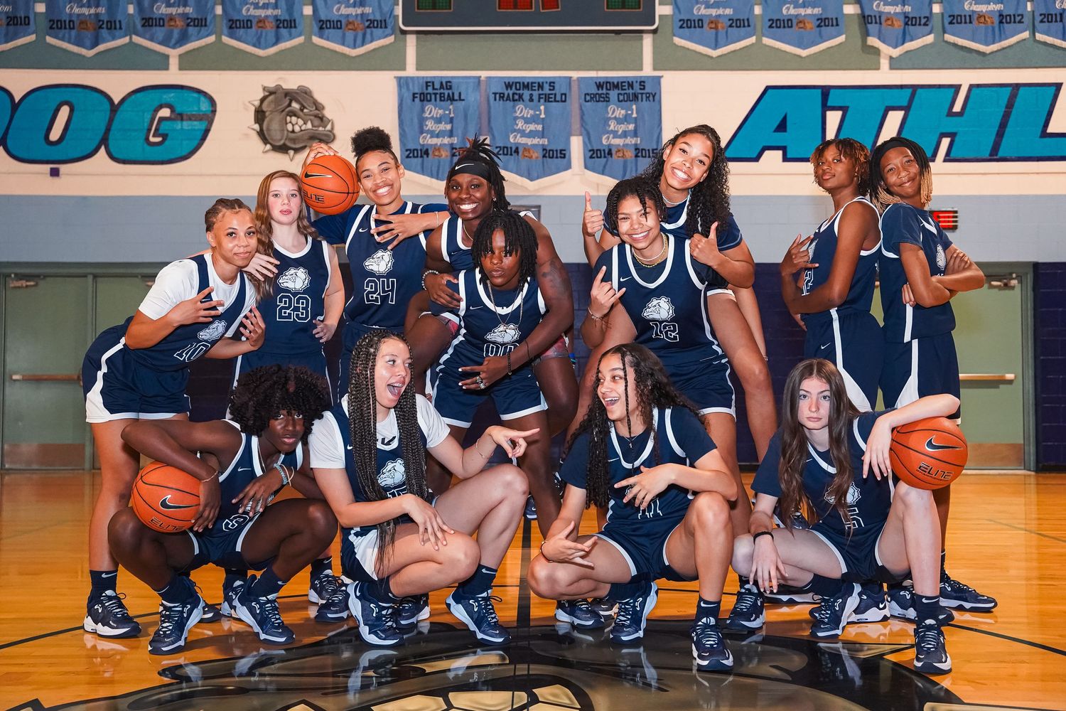 Basketball team in navy uniforms poses playfully on court for team photo.