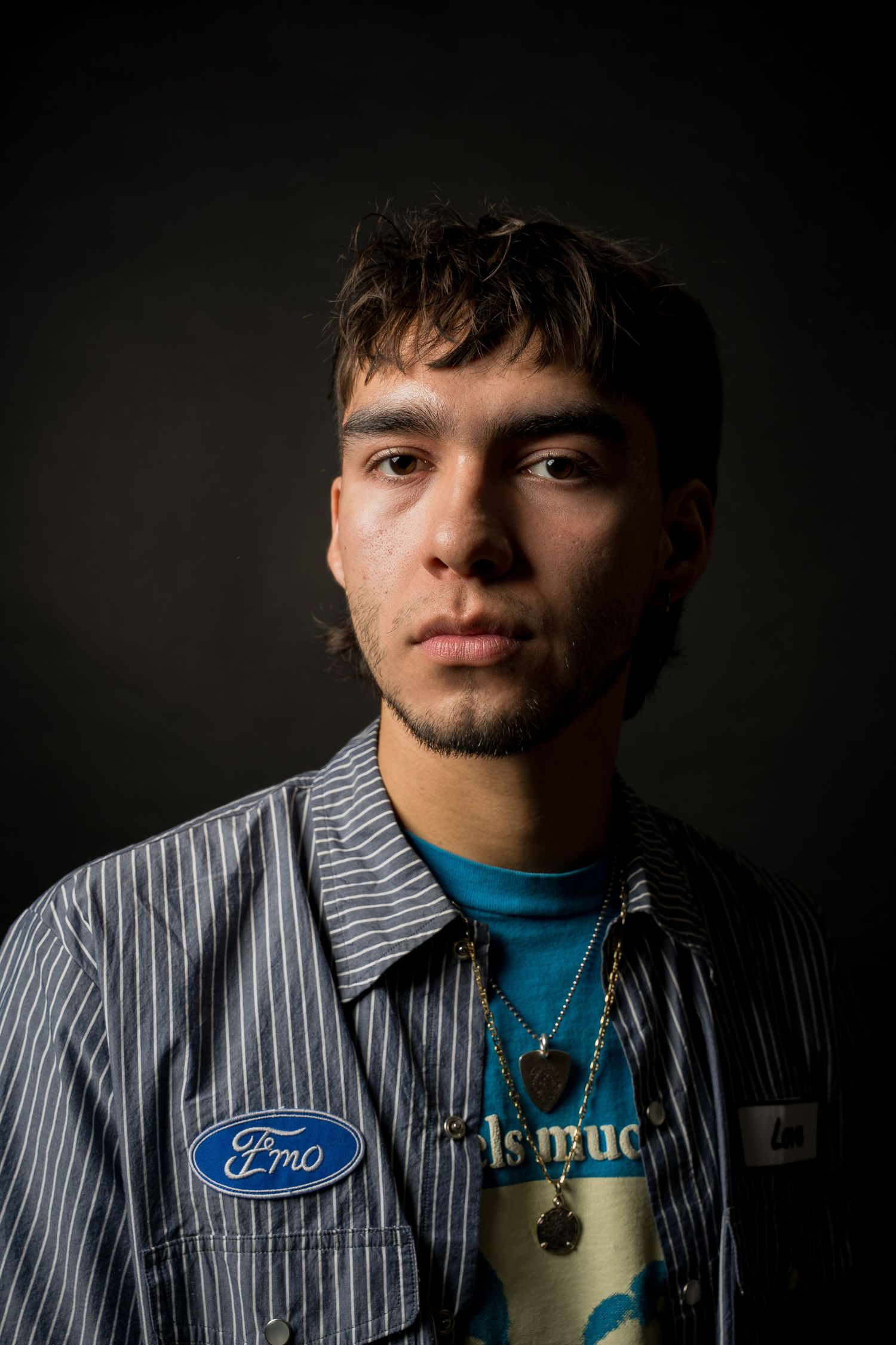 Monaco Media. Moody portrait of a young man in striped work shirt with Ford logo against dark background.