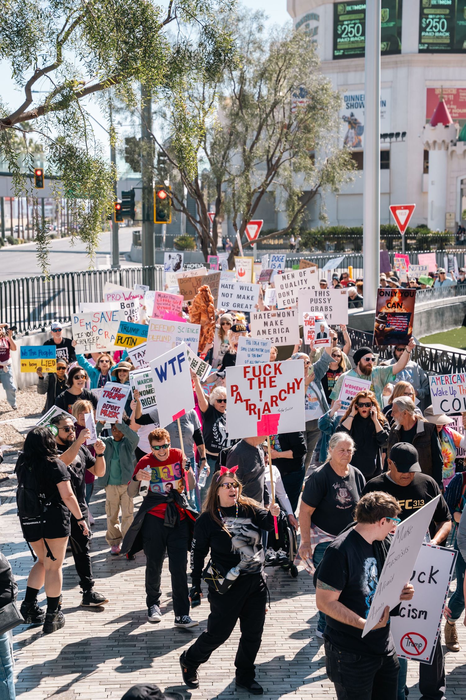 Large crowd of protesters marching with signs along city street during daytime demonstration.