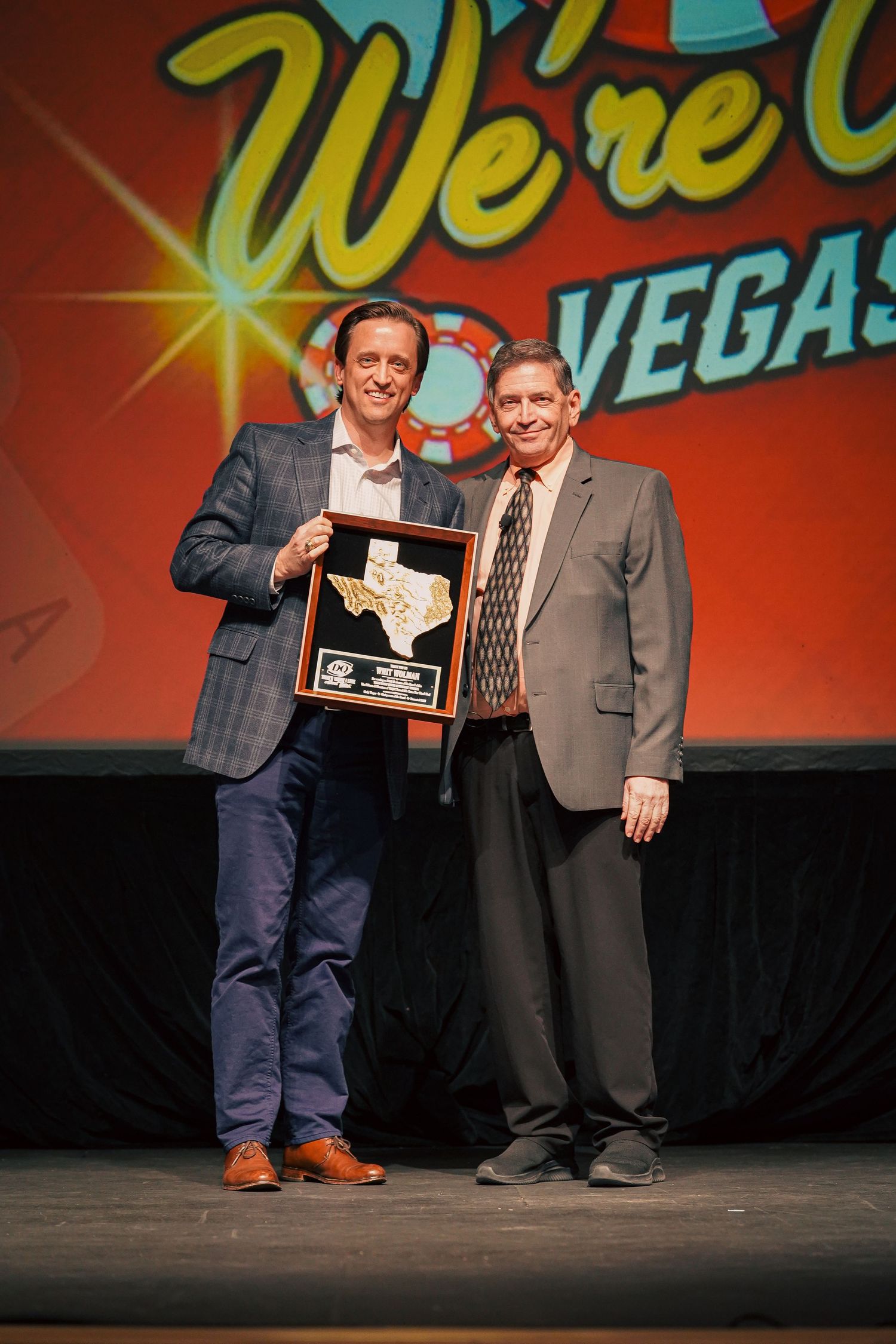 Two men on stage with one holding Texas-shaped award at Vegas event.