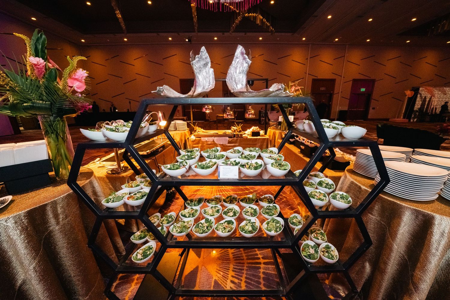 Multi-tiered hexagonal display of elegant appetizers and desserts at upscale catering event.
