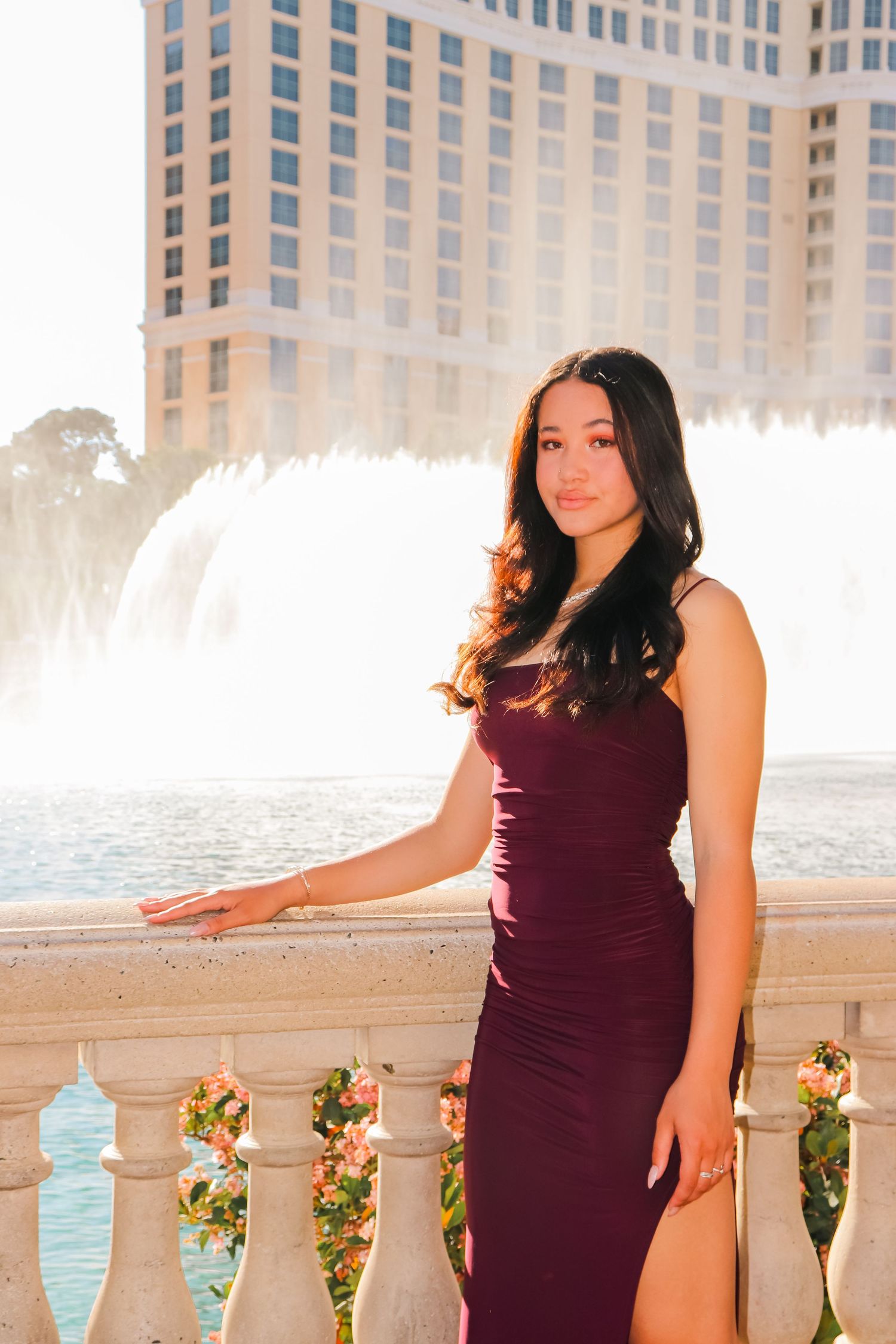 Woman in burgundy dress poses by fountain at luxury hotel.