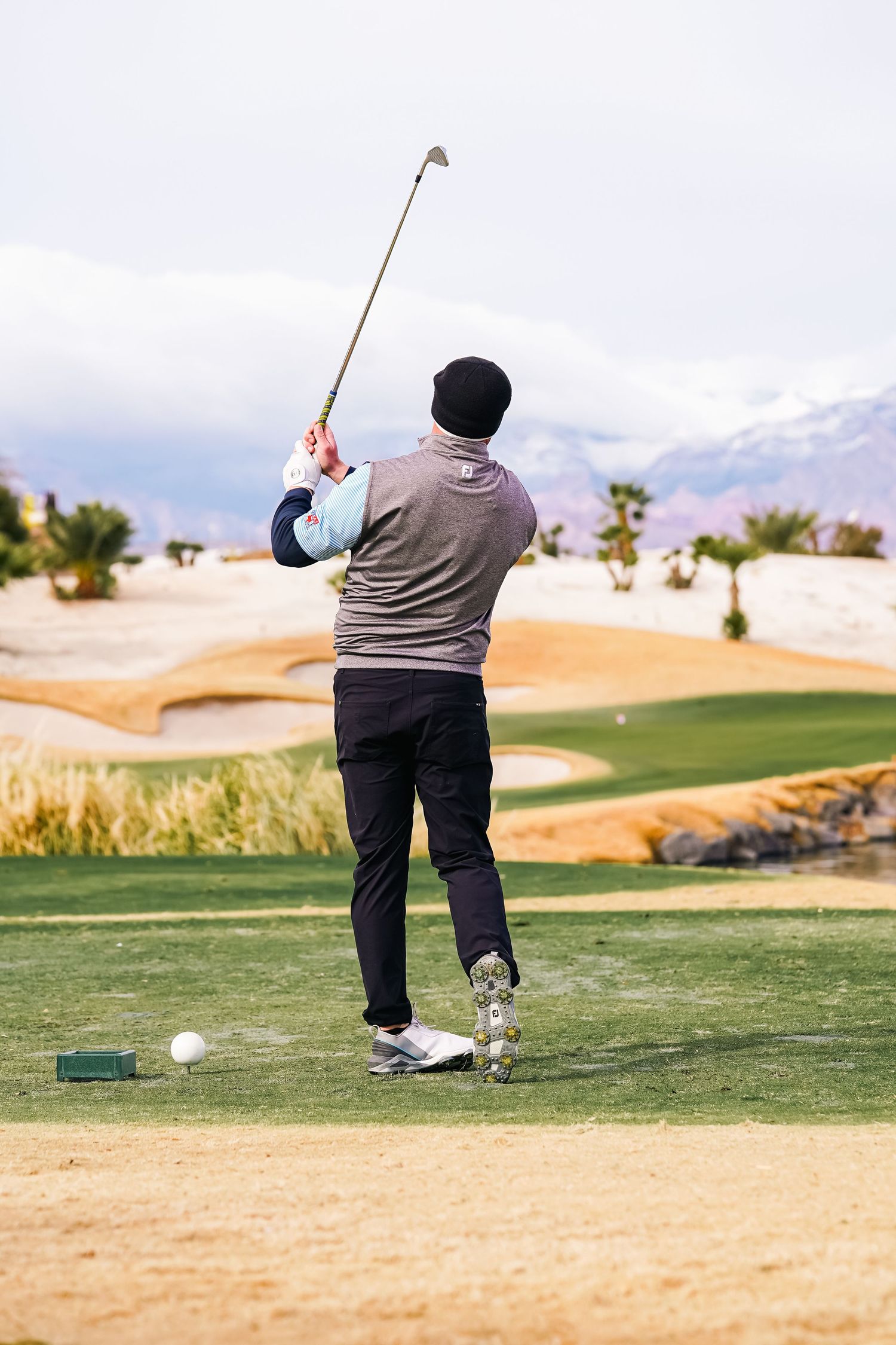 Golfer preparing to tee off with a driver on a desert course.