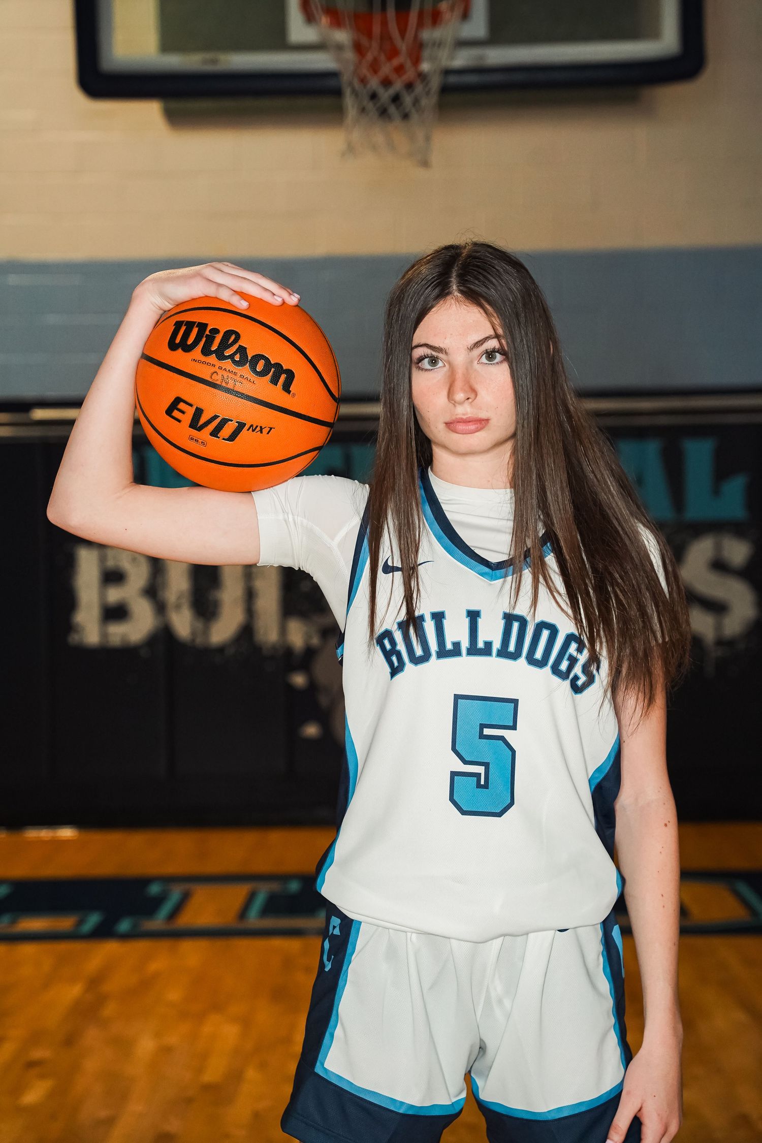 Basketball player in white Bulldogs jersey number 5 poses with Wilson basketball in gym.
