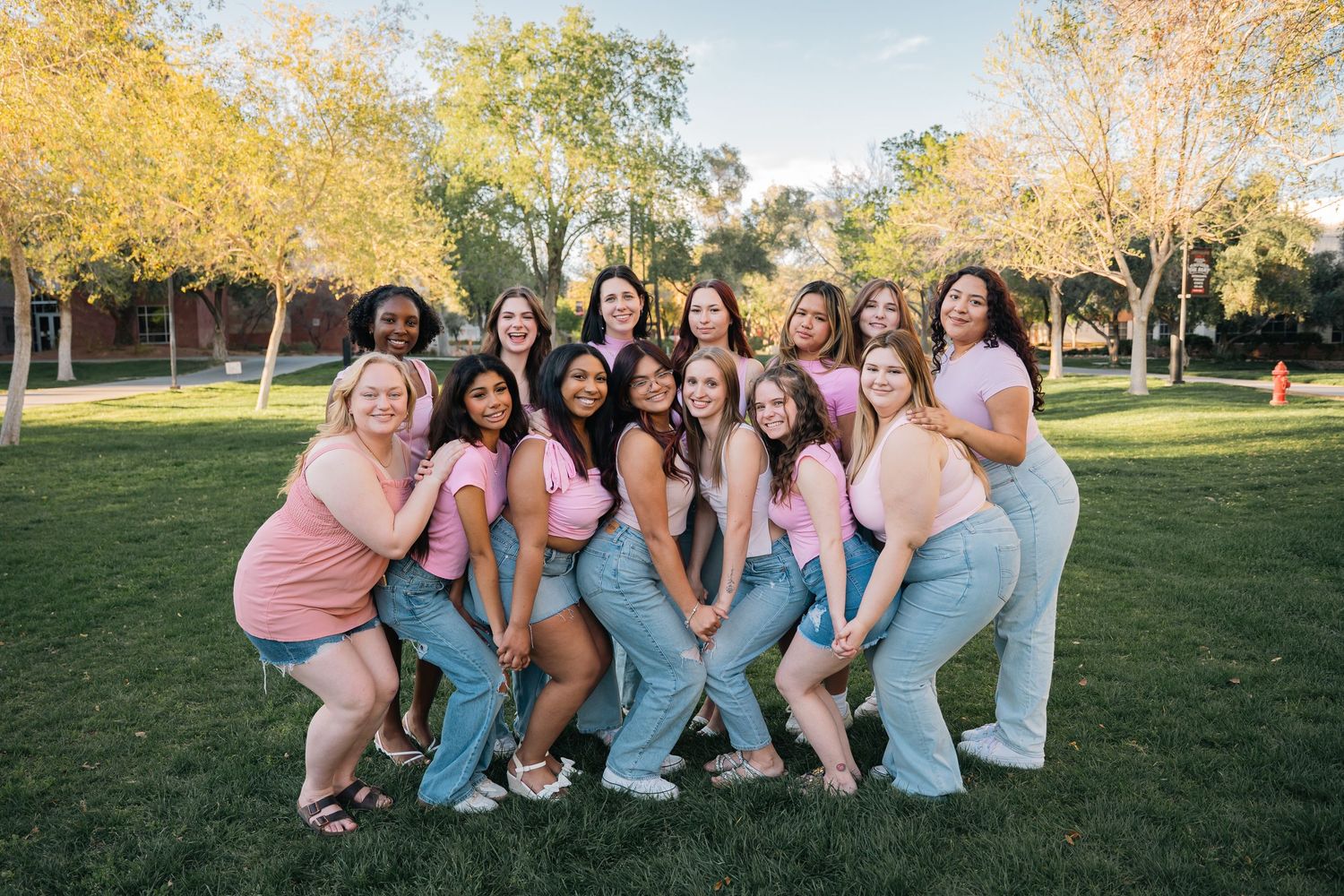 A cheerful group poses in casual outfits on a grassy lawn with autumn trees in the background.