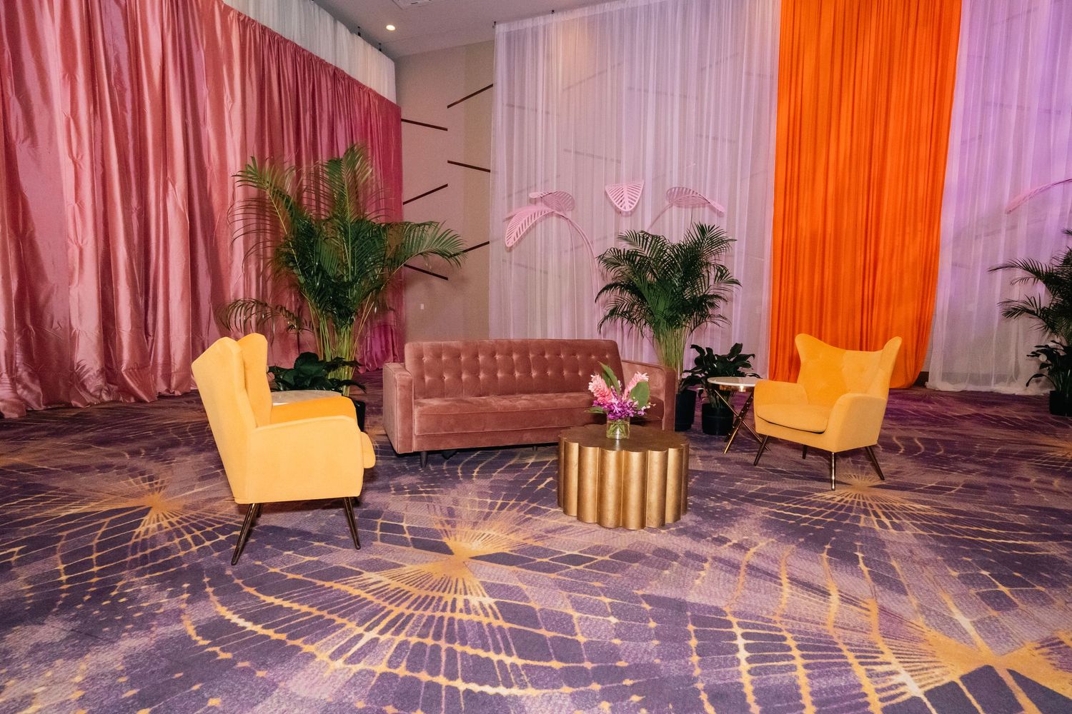 Stylish lounge setup with yellow accent chairs and pink drapes against a geometric patterned floor.