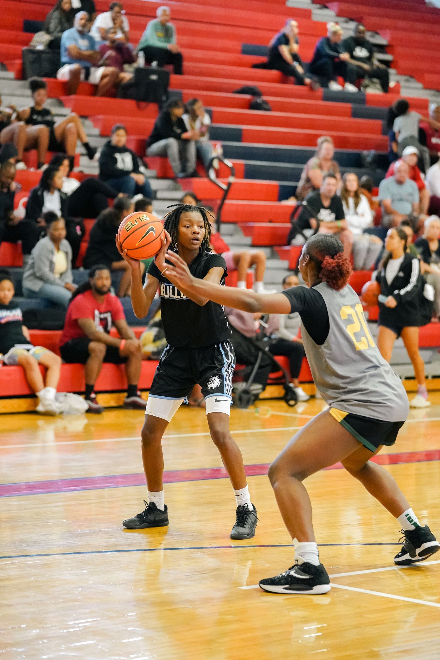 Basketball player protects ball while defender guards during game on red court.