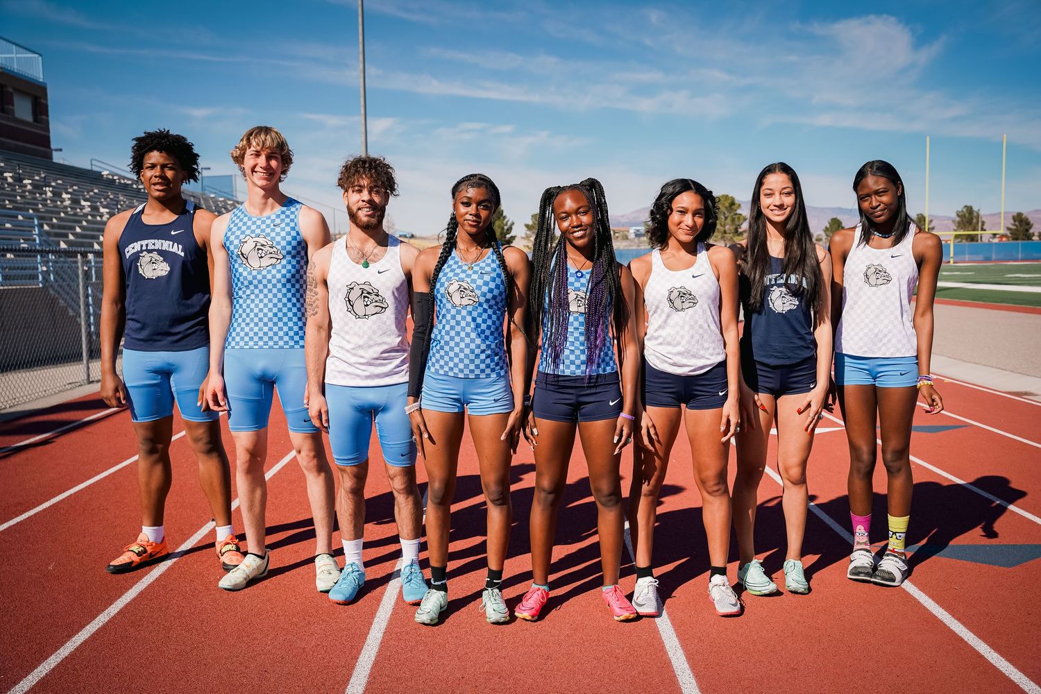 Track team members lined up together on red running track wearing team uniforms.