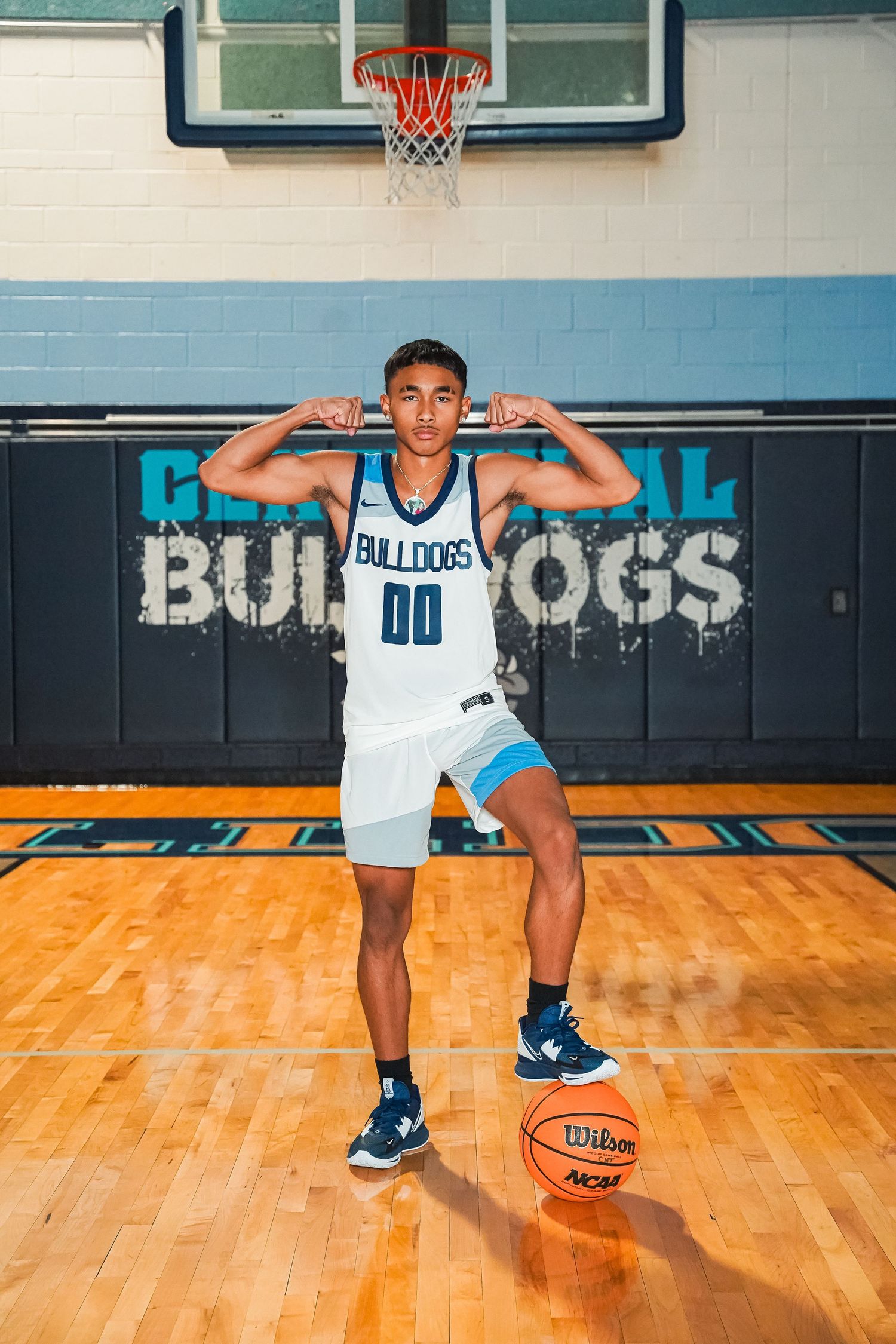 Basketball player in Bulldogs uniform posing with basketball on wooden court.