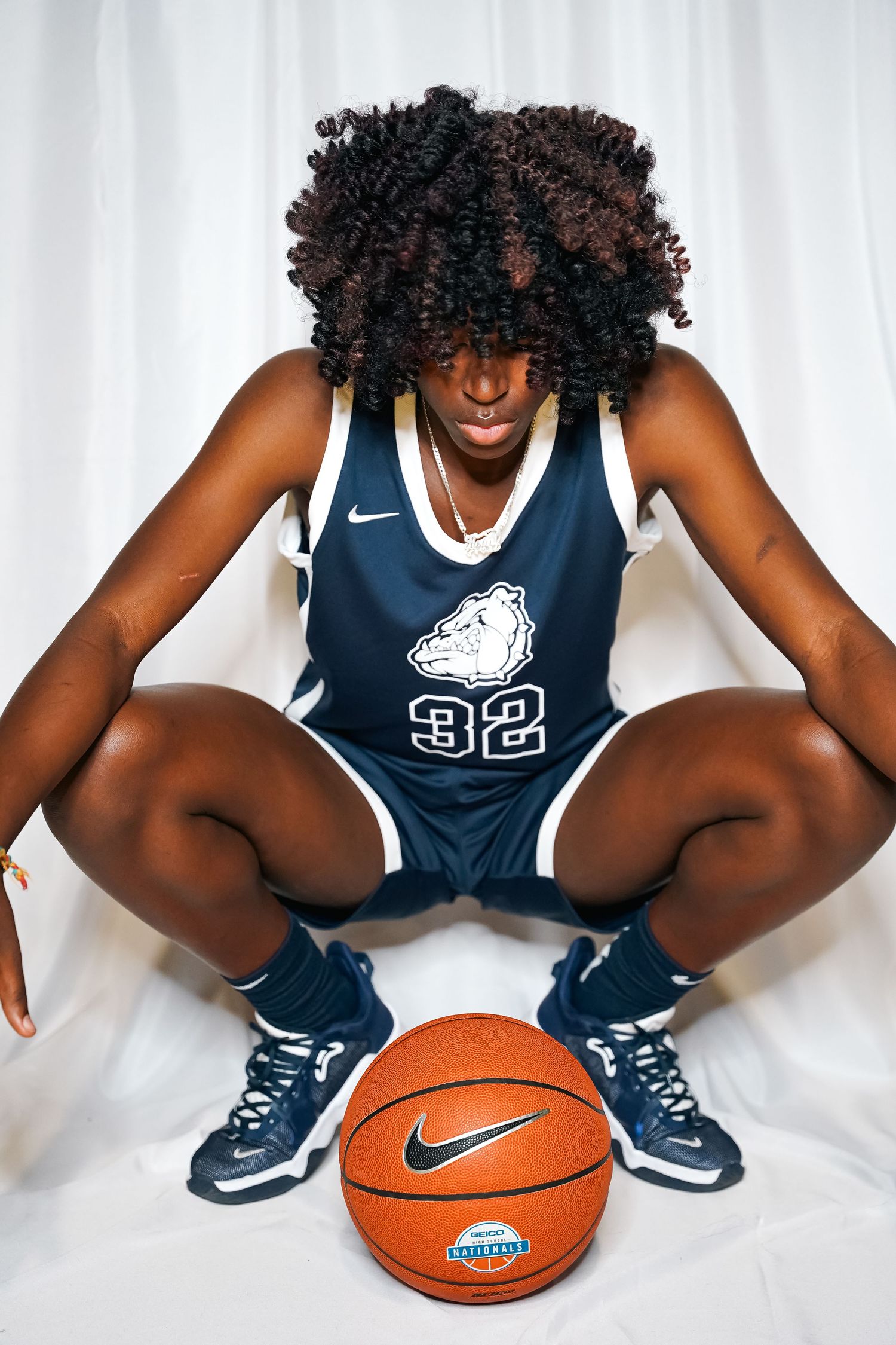 Basketball player in navy uniform poses with ball against white backdrop.