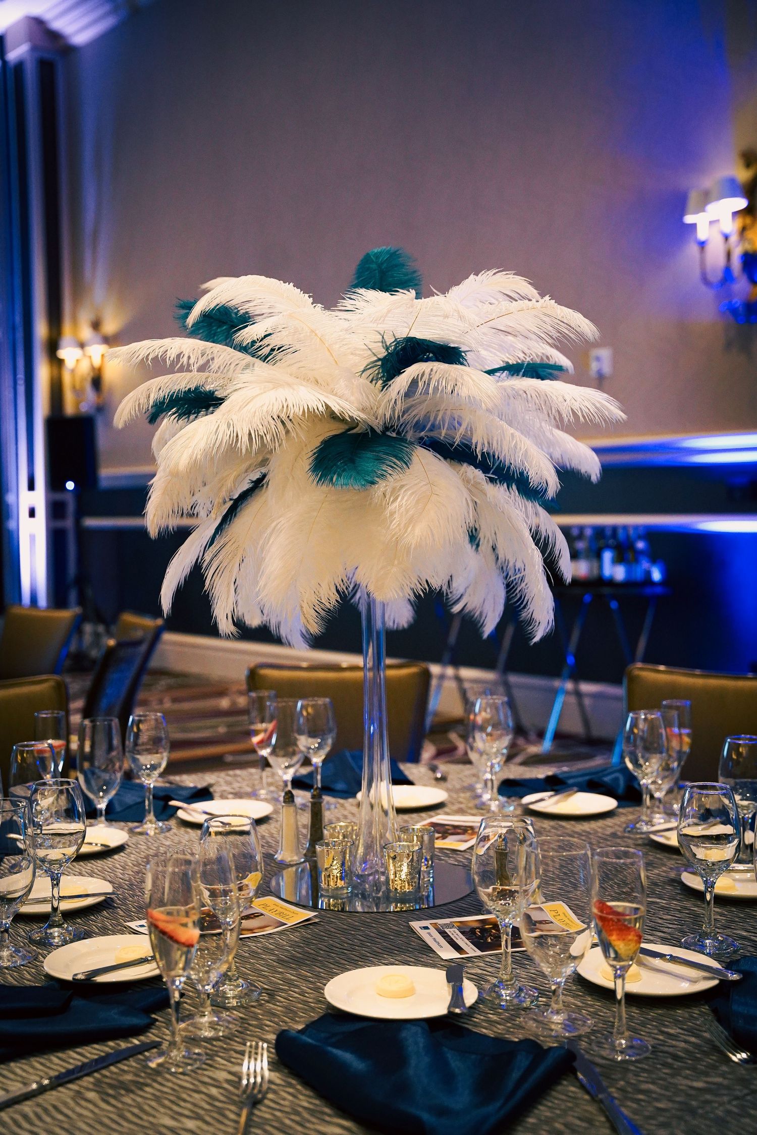 Dramatic white feather and teal centerpiece display on formal dinner table setting.