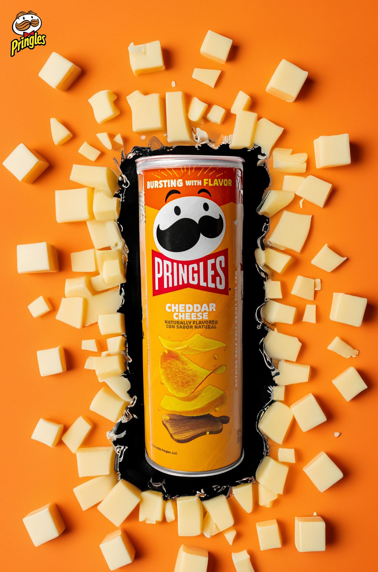 Cheddar Pringles can surrounded by cheese cubes on vibrant orange background.