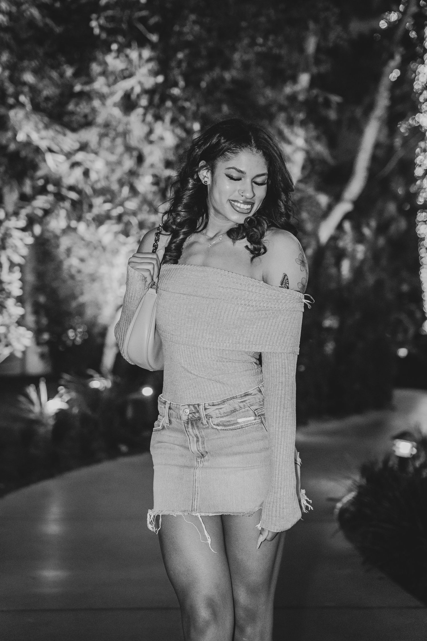 Black and white candid fashion photo with off-shoulder sweater in garden setting.