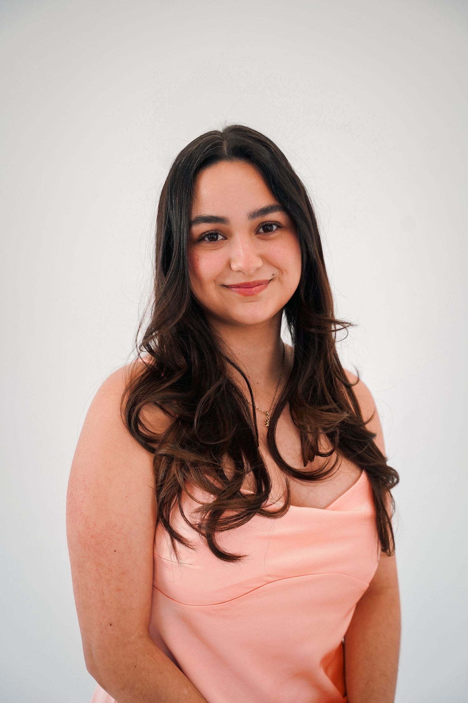 Woman in coral pink camisole poses against white studio backdrop.
