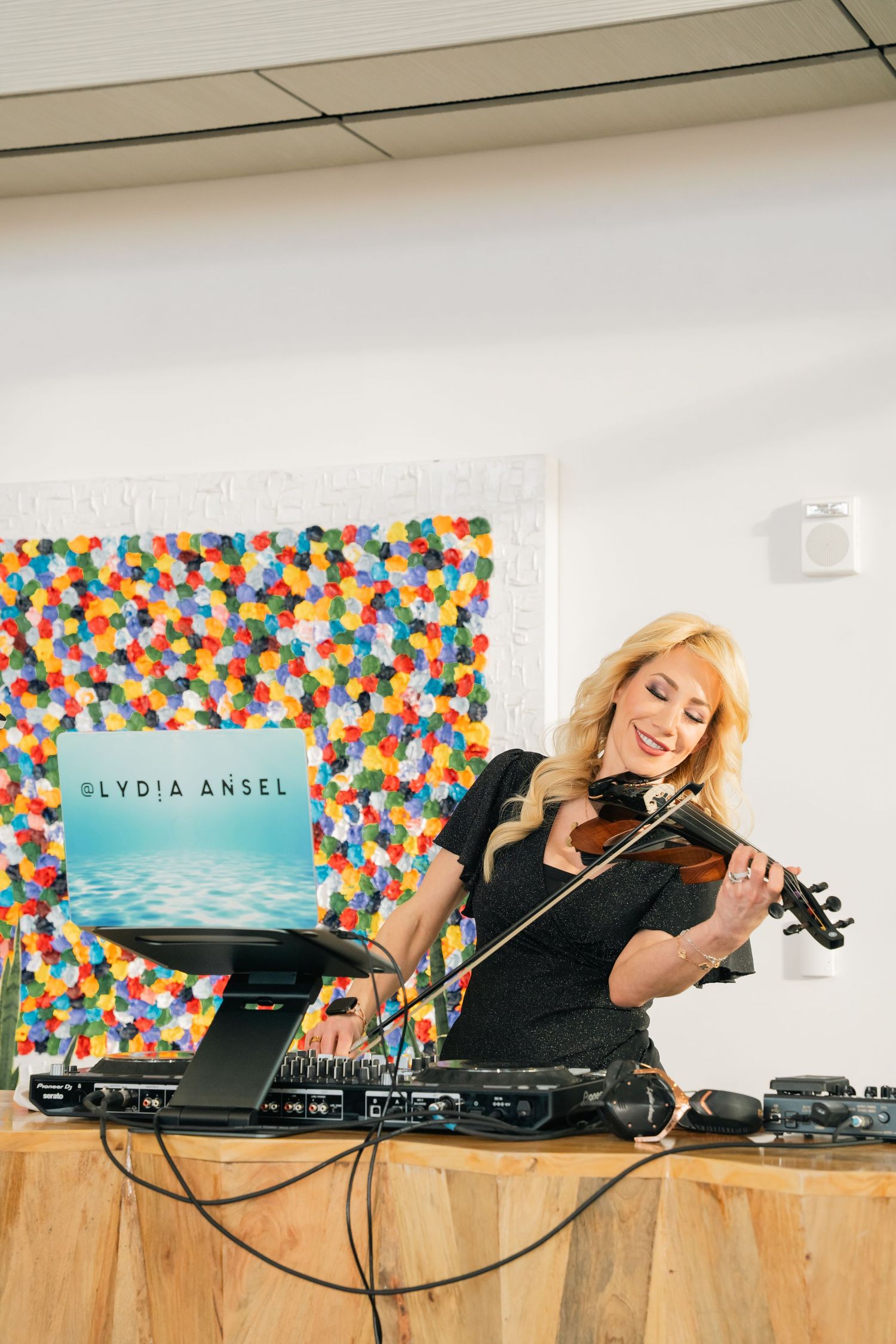 Musician performing with a violin against a colorful polka dot backdrop.