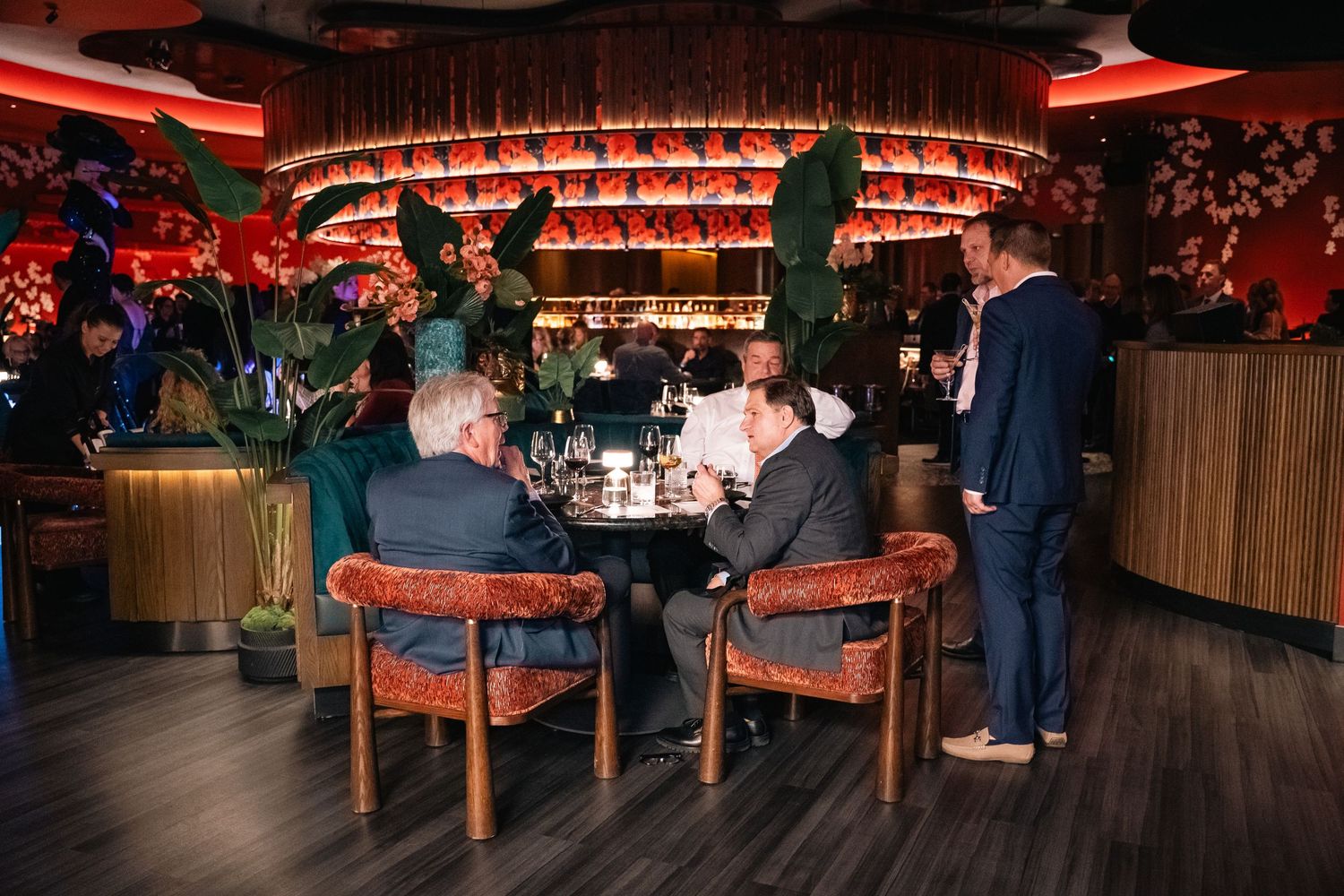 Diners seated at wooden tables beneath red ceiling decor in an upscale restaurant.