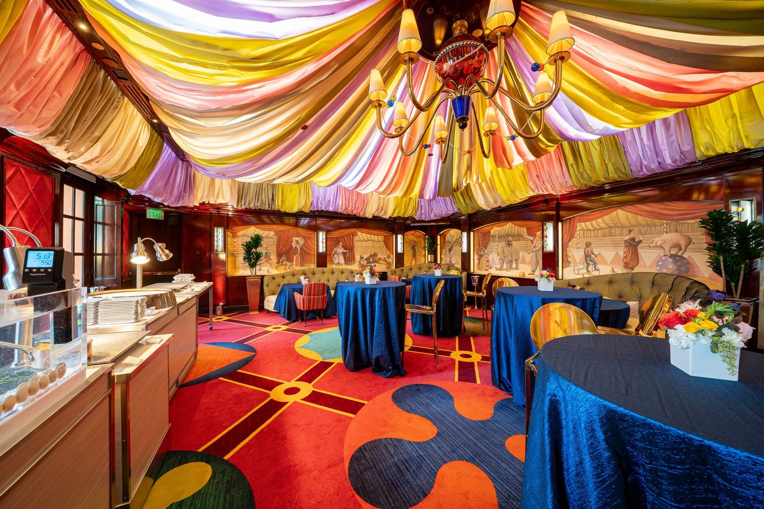 Colorful draped ceiling with blue tablecloths and red carpet in an elegant event space.