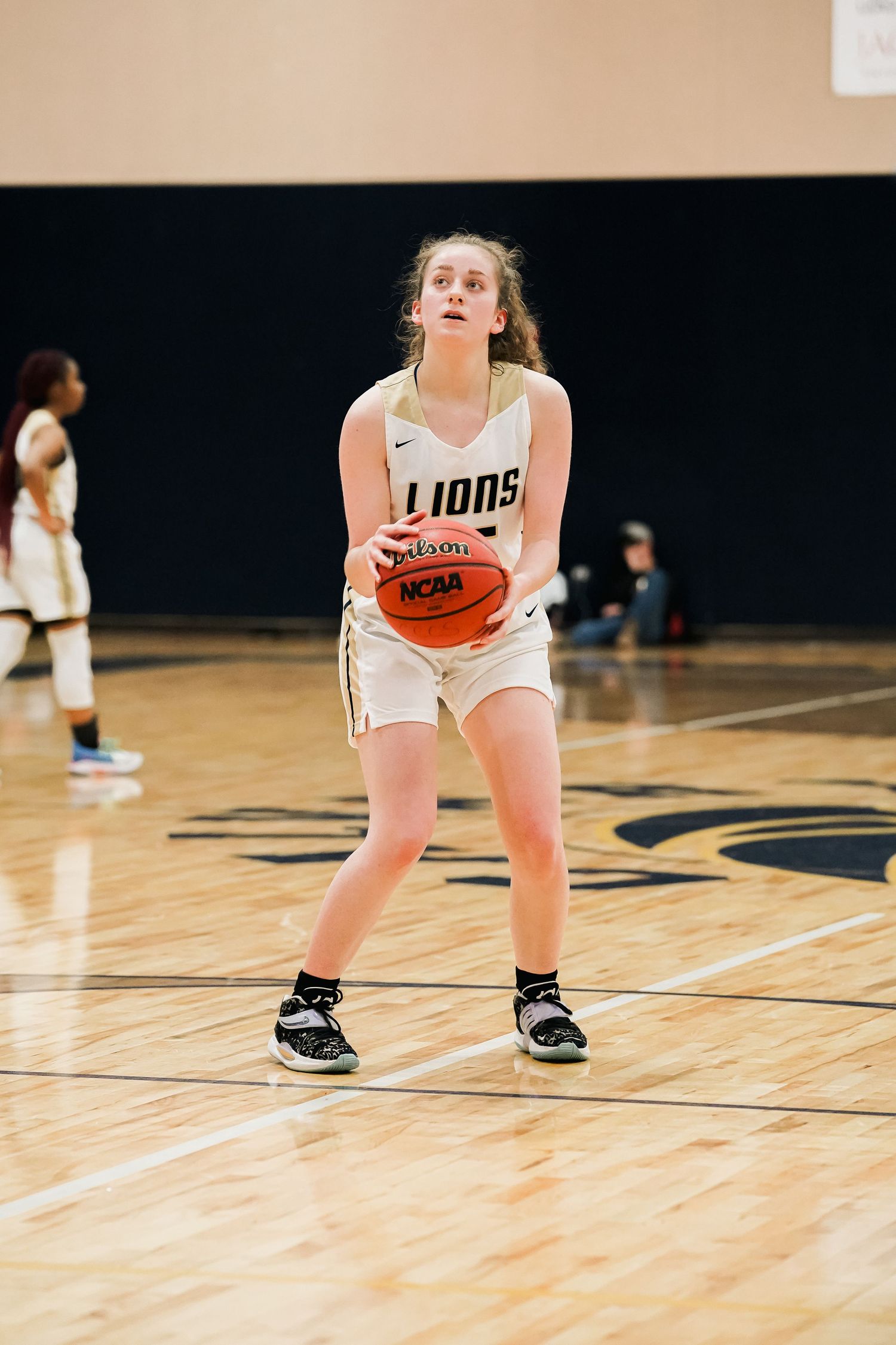 Basketball player in white Lions uniform crouching low while dribbling.