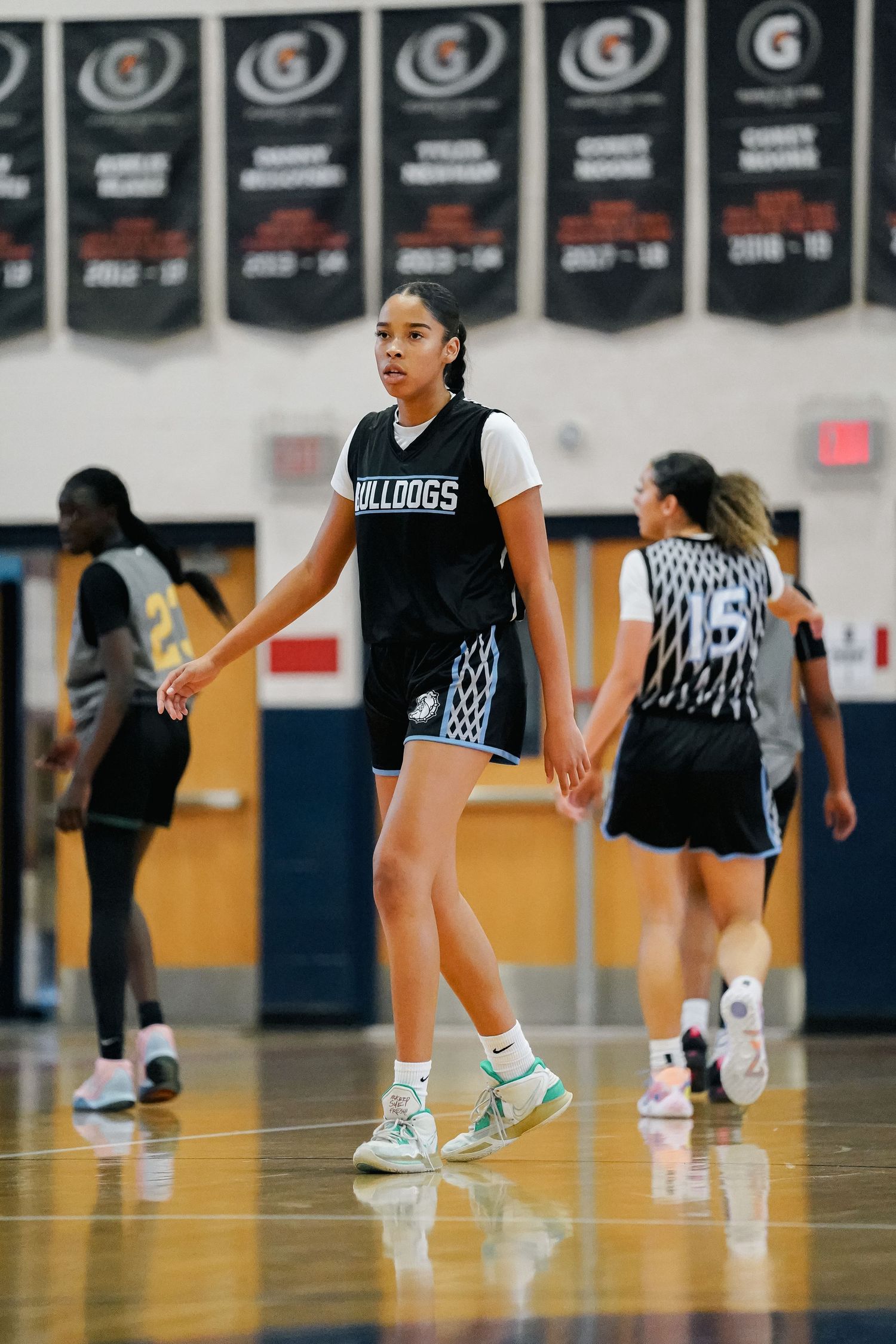 Basketball players in black uniforms spread across the court during practice drills.
