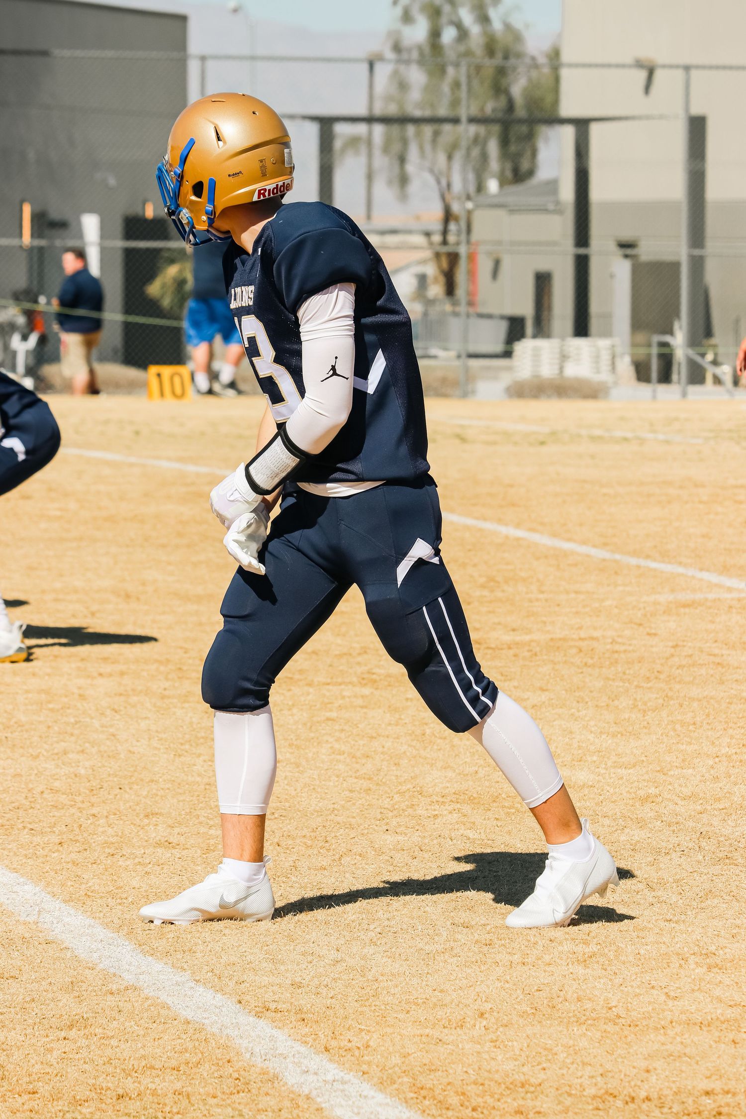 Player in navy uniform with gold helmet stands ready on football field.