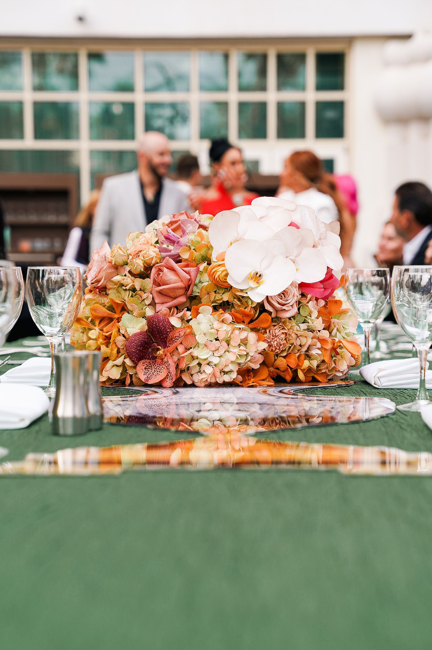 Floral centerpiece with pink and orange flowers arranged on green tablecloth at wedding reception.