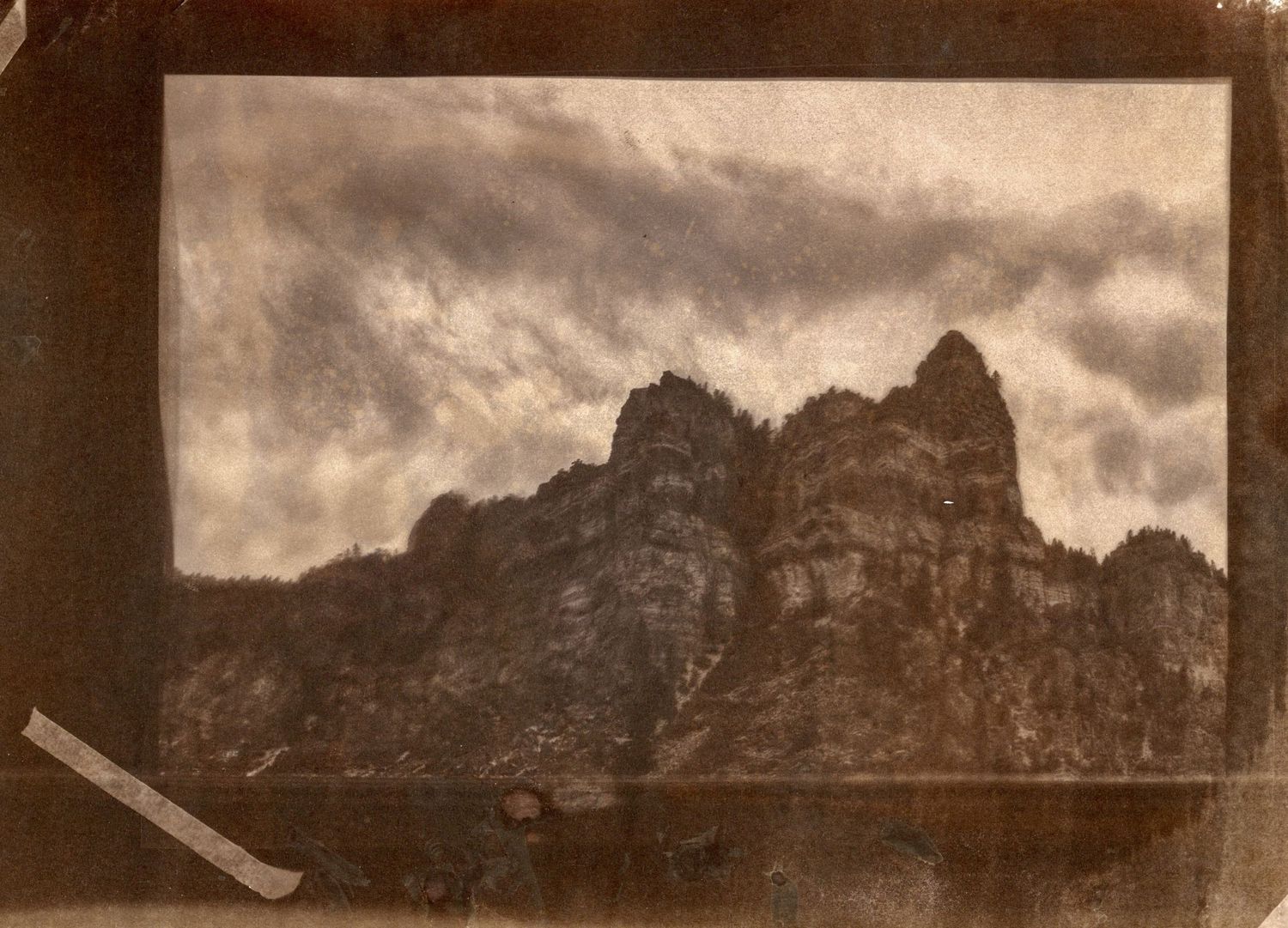Sepia landscape photograph of jagged mountain peaks under dramatic cloudy skies.