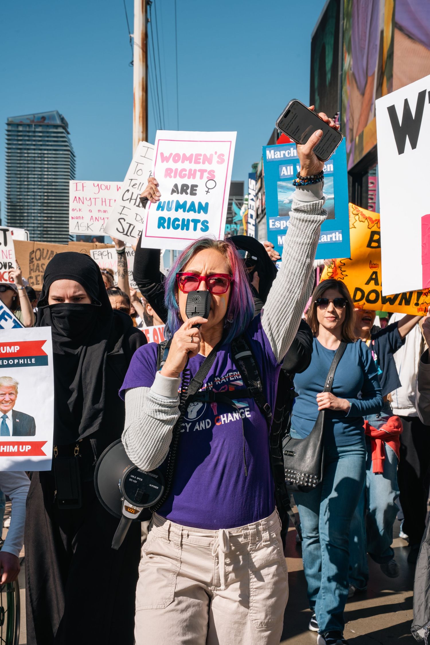 Protesters with signs and megaphones gather at street demonstration for human rights.