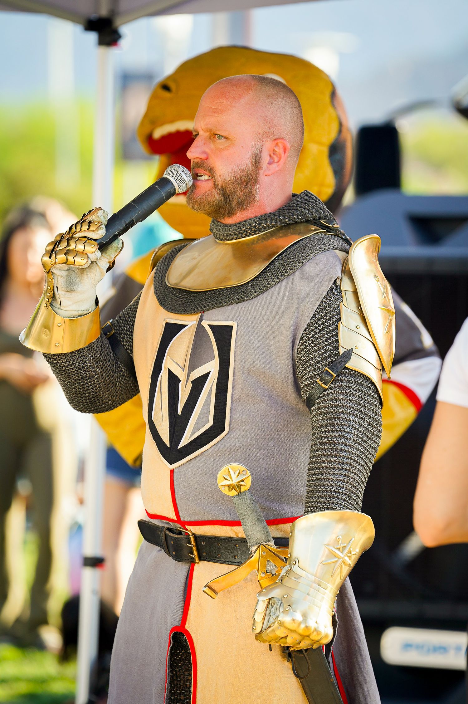 Costumed performer in knight armor holds microphone while wearing Vegas Golden Knights logo.