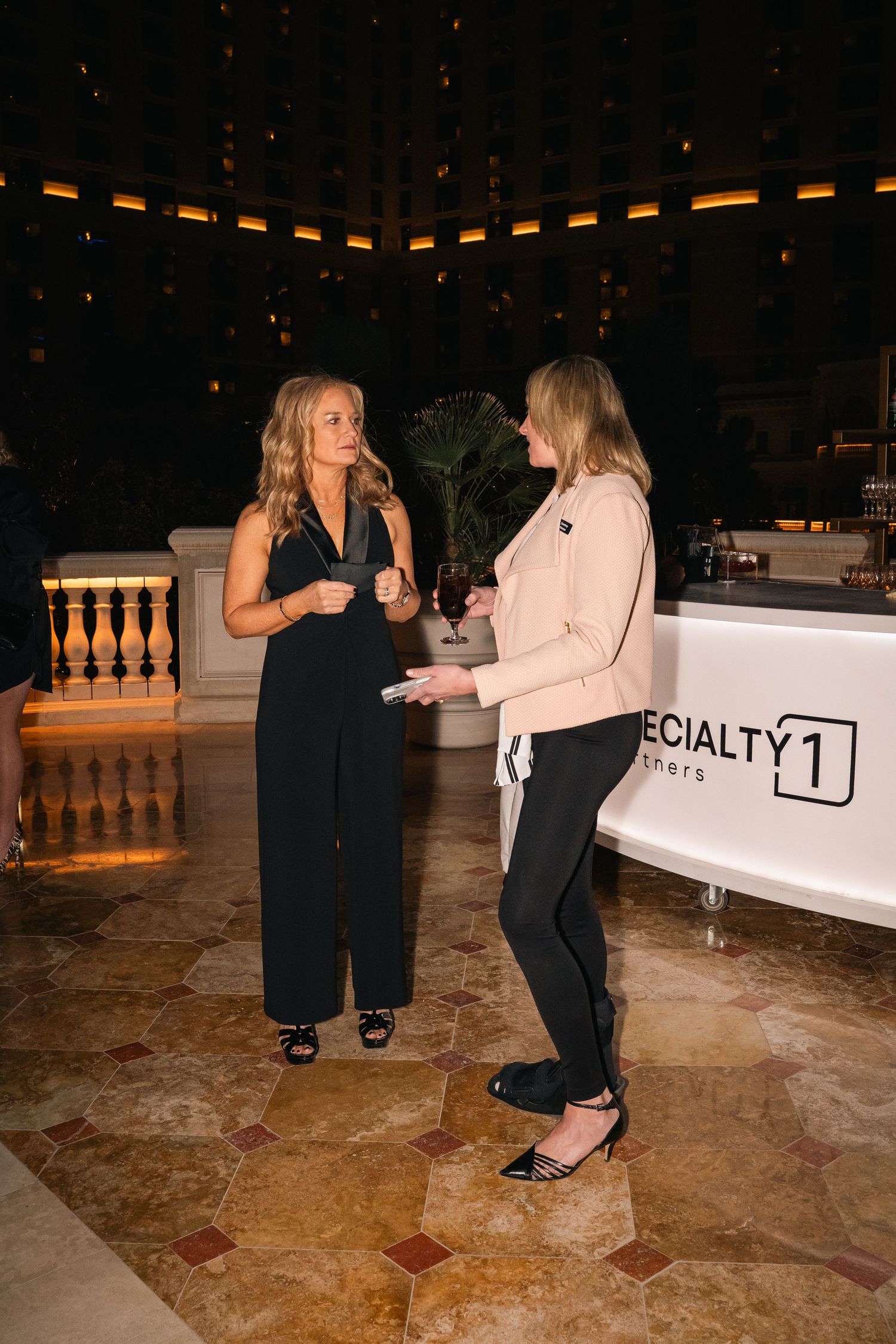 Two guests in business attire having conversation near Specialty1 branded banner at evening event.