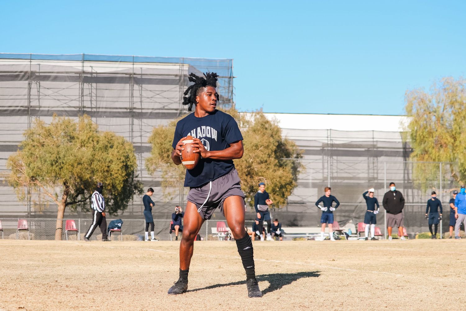 Football player in navy uniform practicing passing drills on dry grass field.