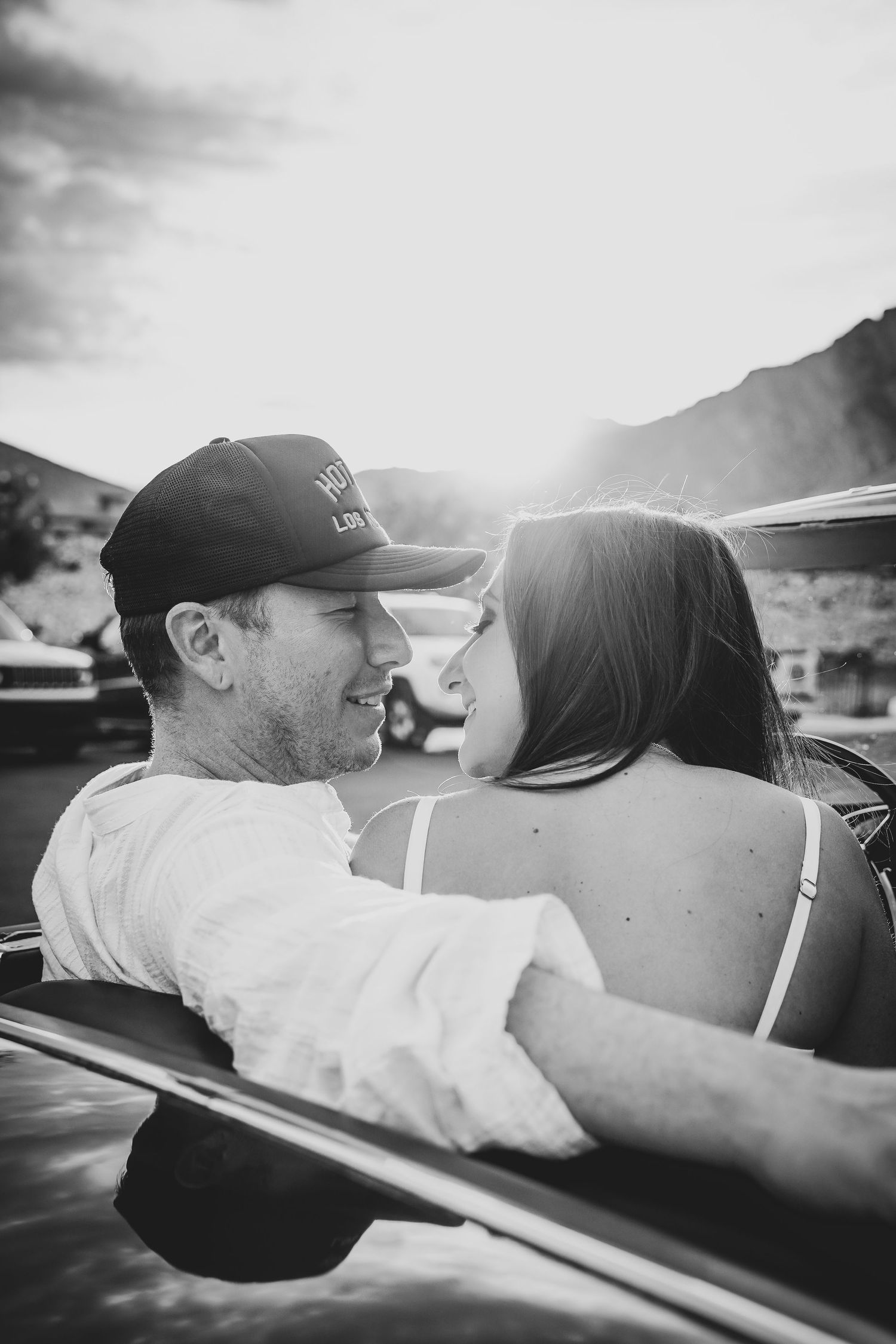 Black and white photo of couple sharing intimate moment in classic convertible car.