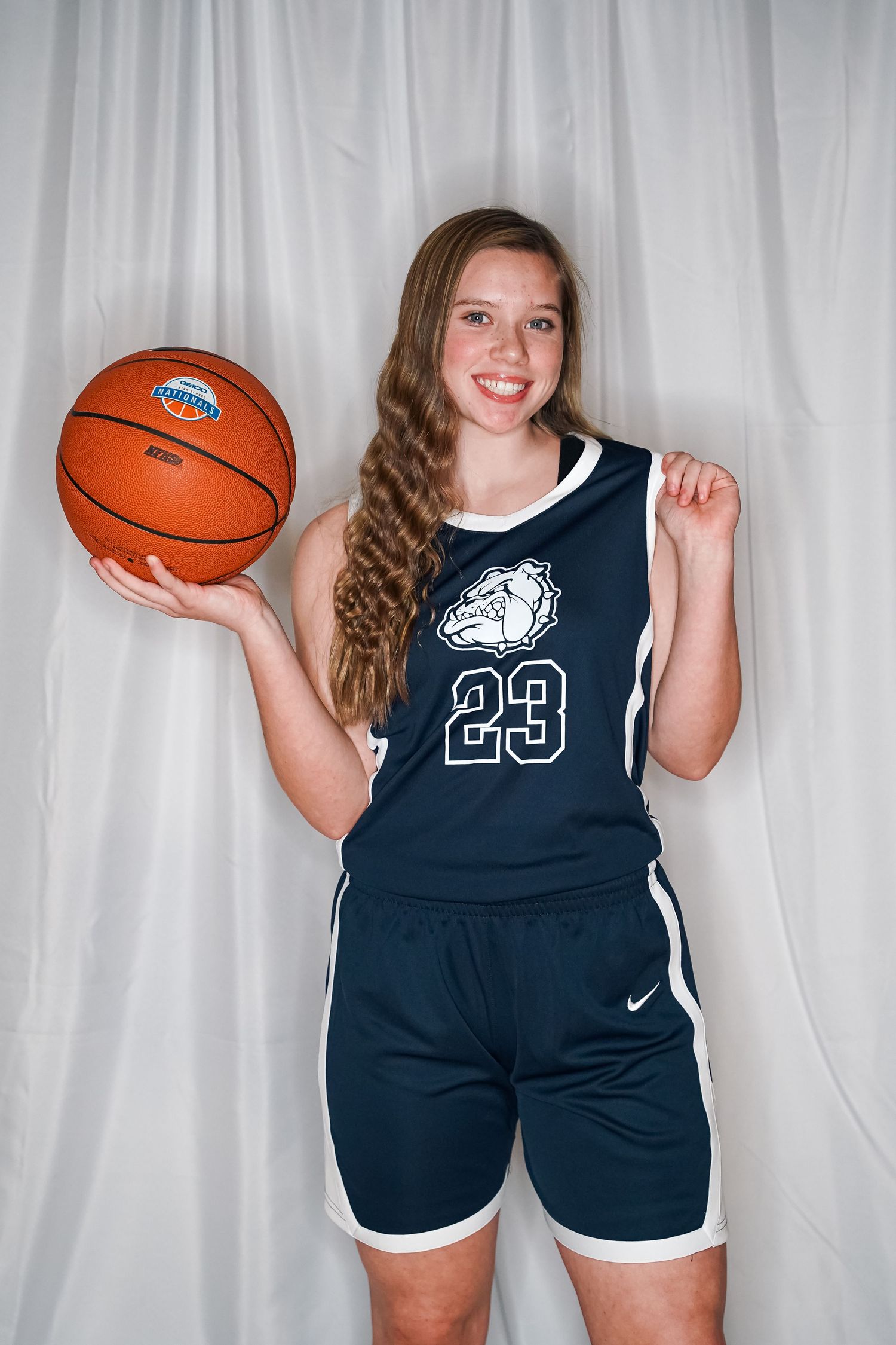 Basketball player in navy uniform holds orange ball against white backdrop.