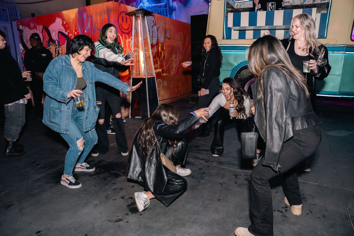 Energetic crowd dancing at nightclub with colorful lighting and urban decor.