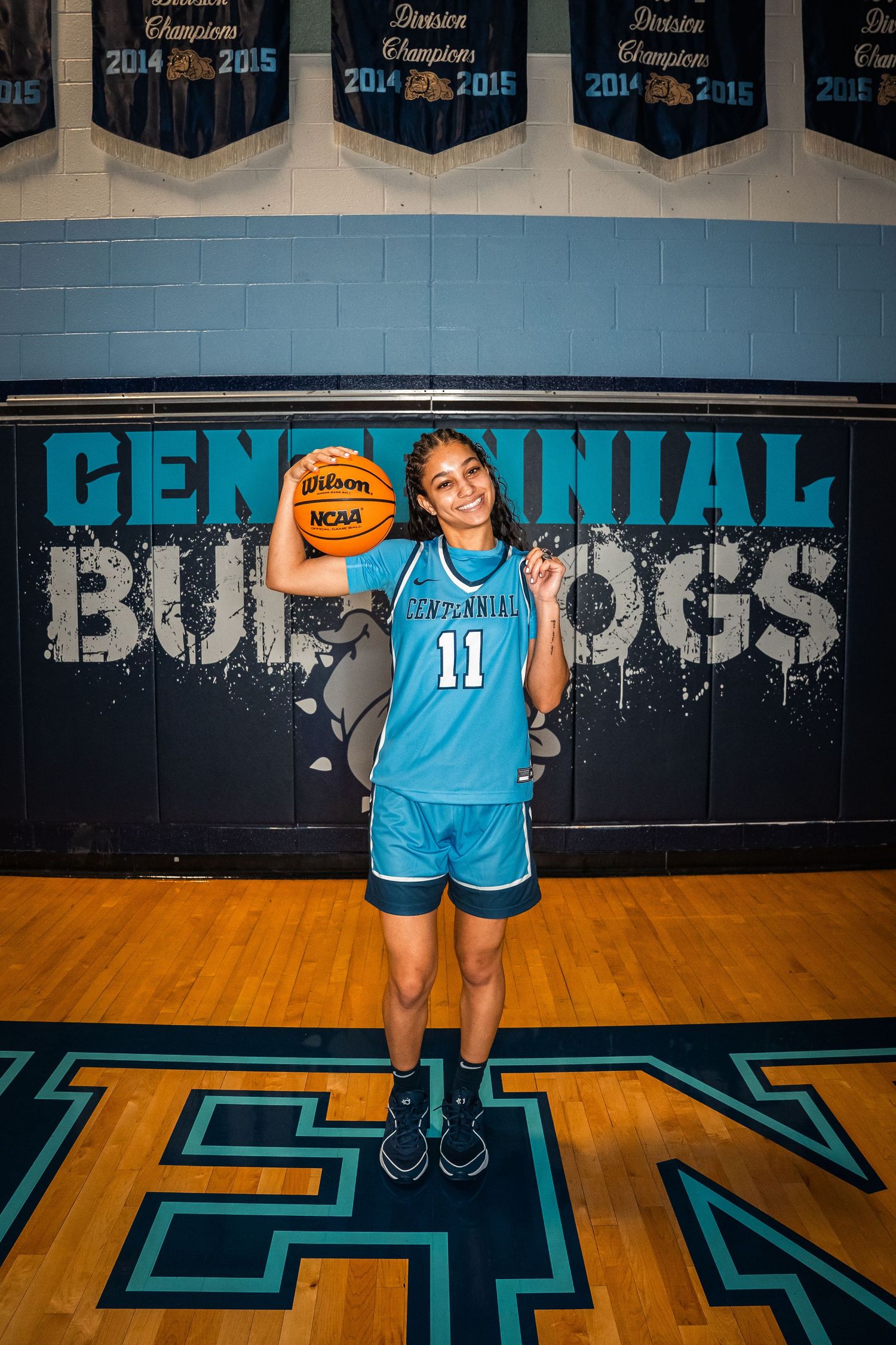 Basketball player in light blue jersey holding ball against team wall display.