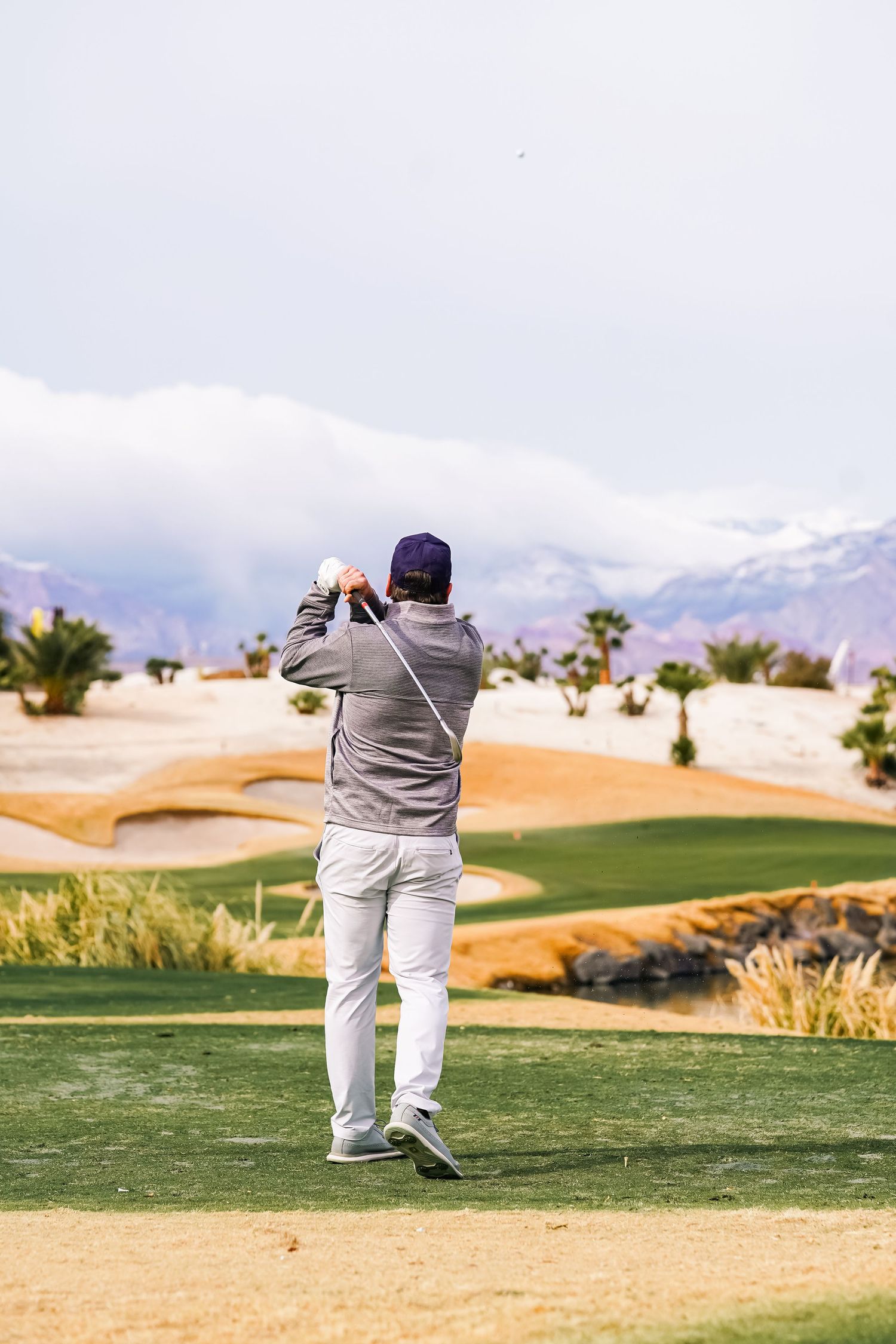 Golfer taking a swing on a desert golf course with mountains in the background.