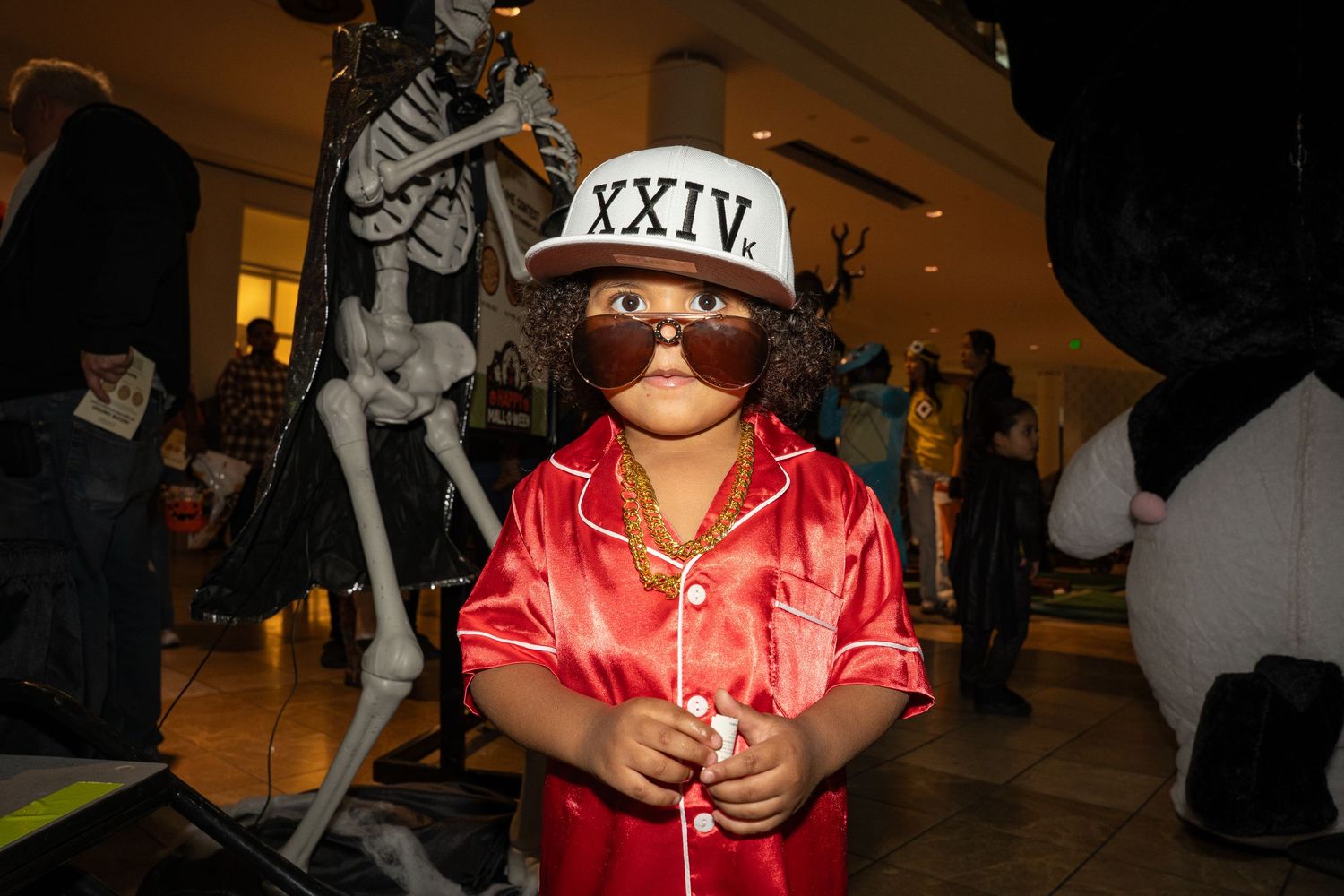 Figure in red satin shirt and baseball cap poses during Halloween festivities.