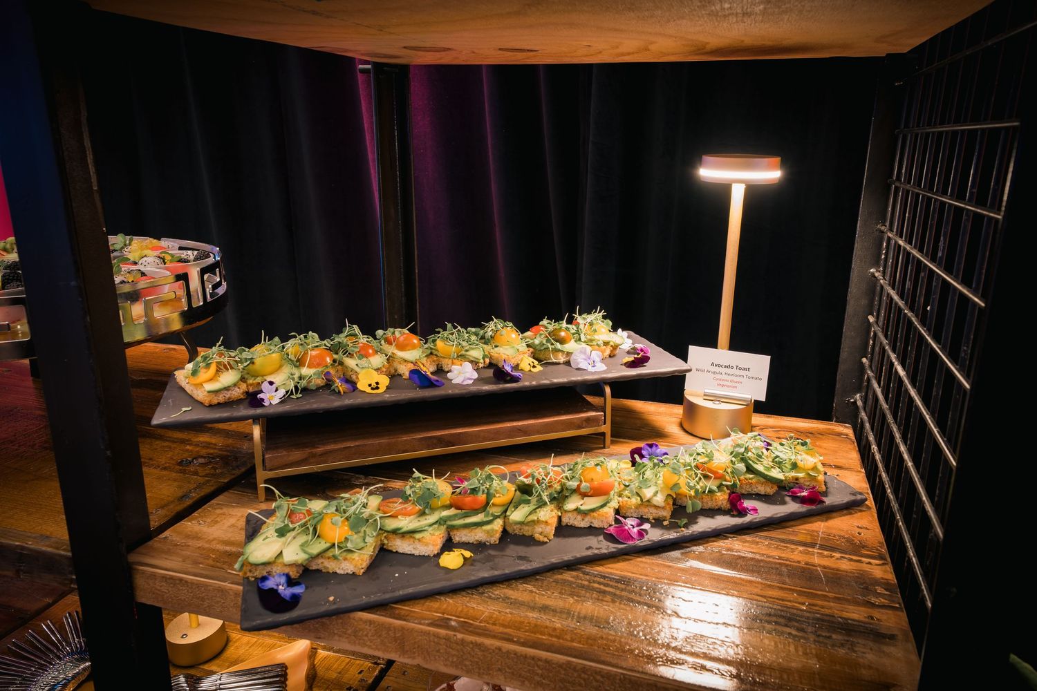 Elevated wooden platforms displaying rows of elegant appetizers in moody restaurant lighting.