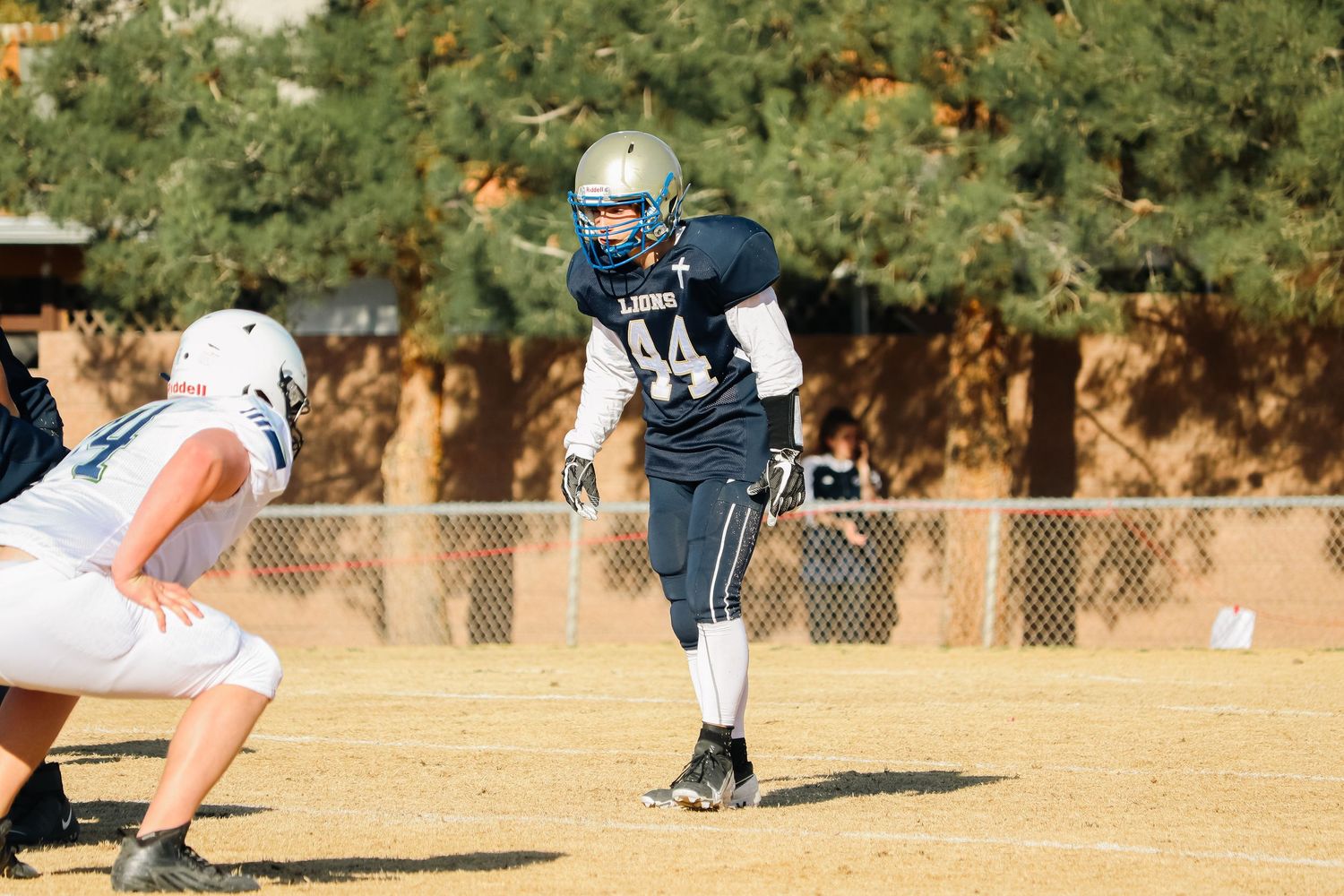 Football players from opposing teams face off during practice on sunny field.