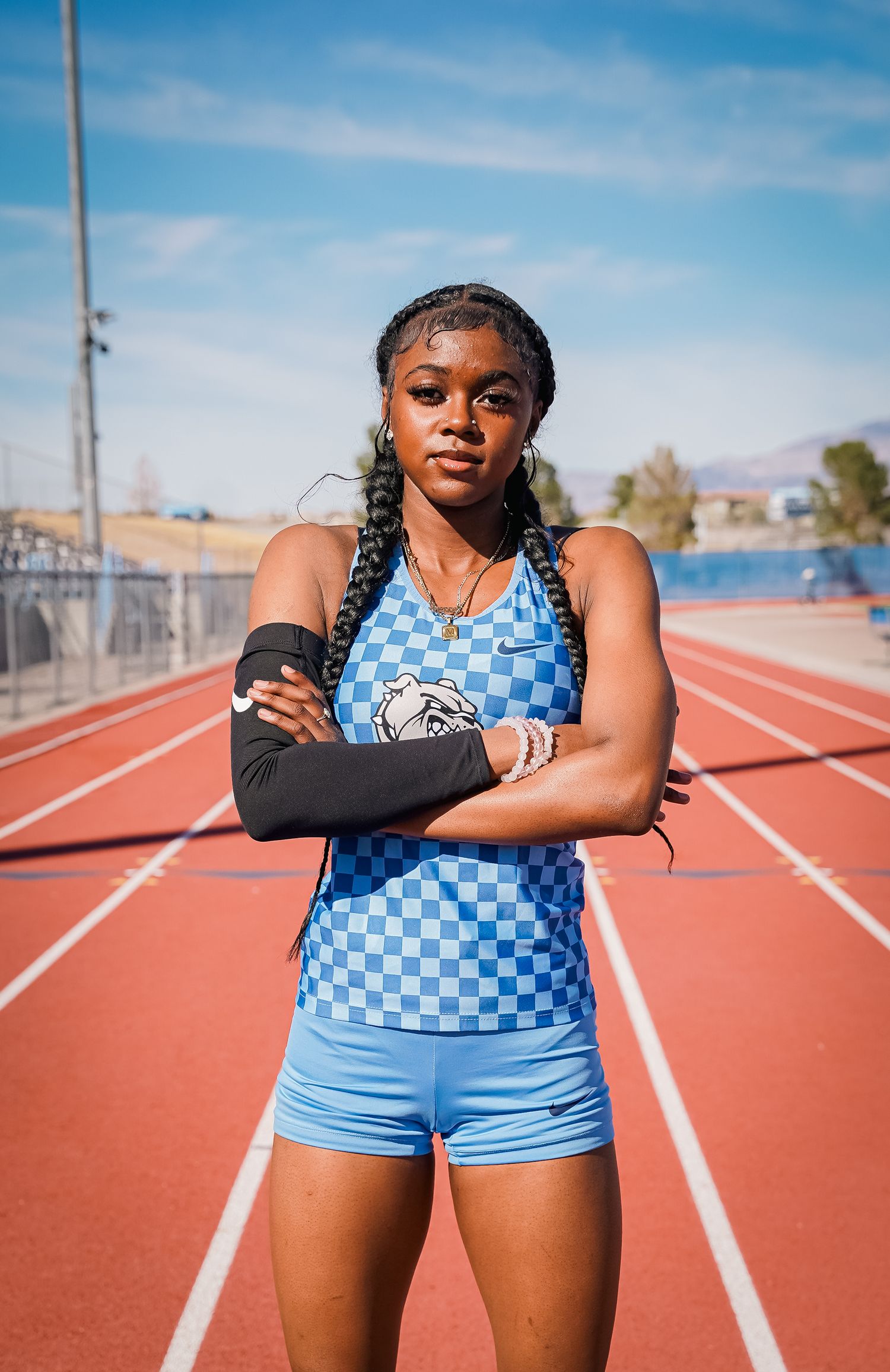 Athlete in blue checkered uniform stands with crossed arms on outdoor track field.